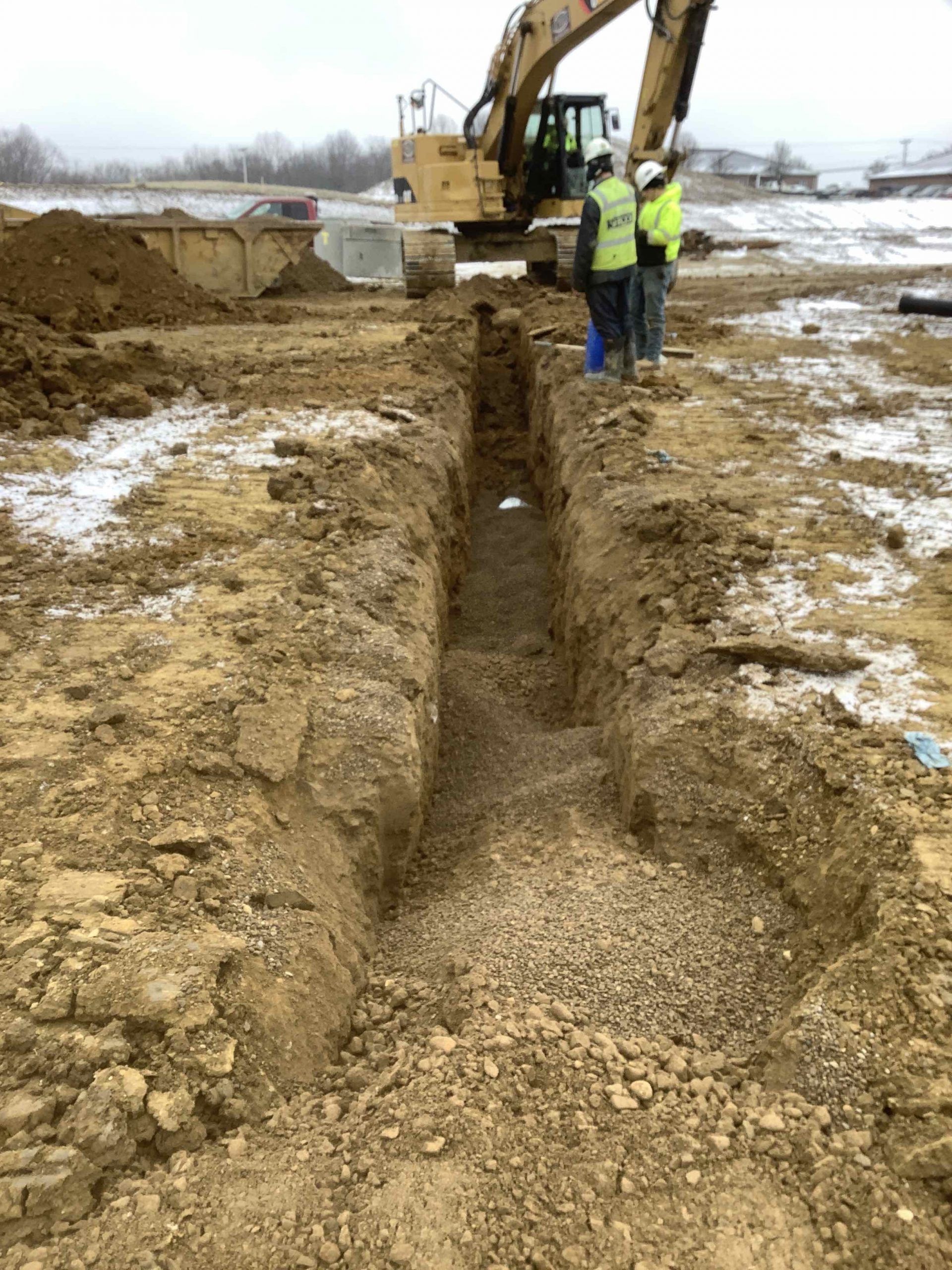 A group of construction workers are standing next to a large excavator in a dirt field.
