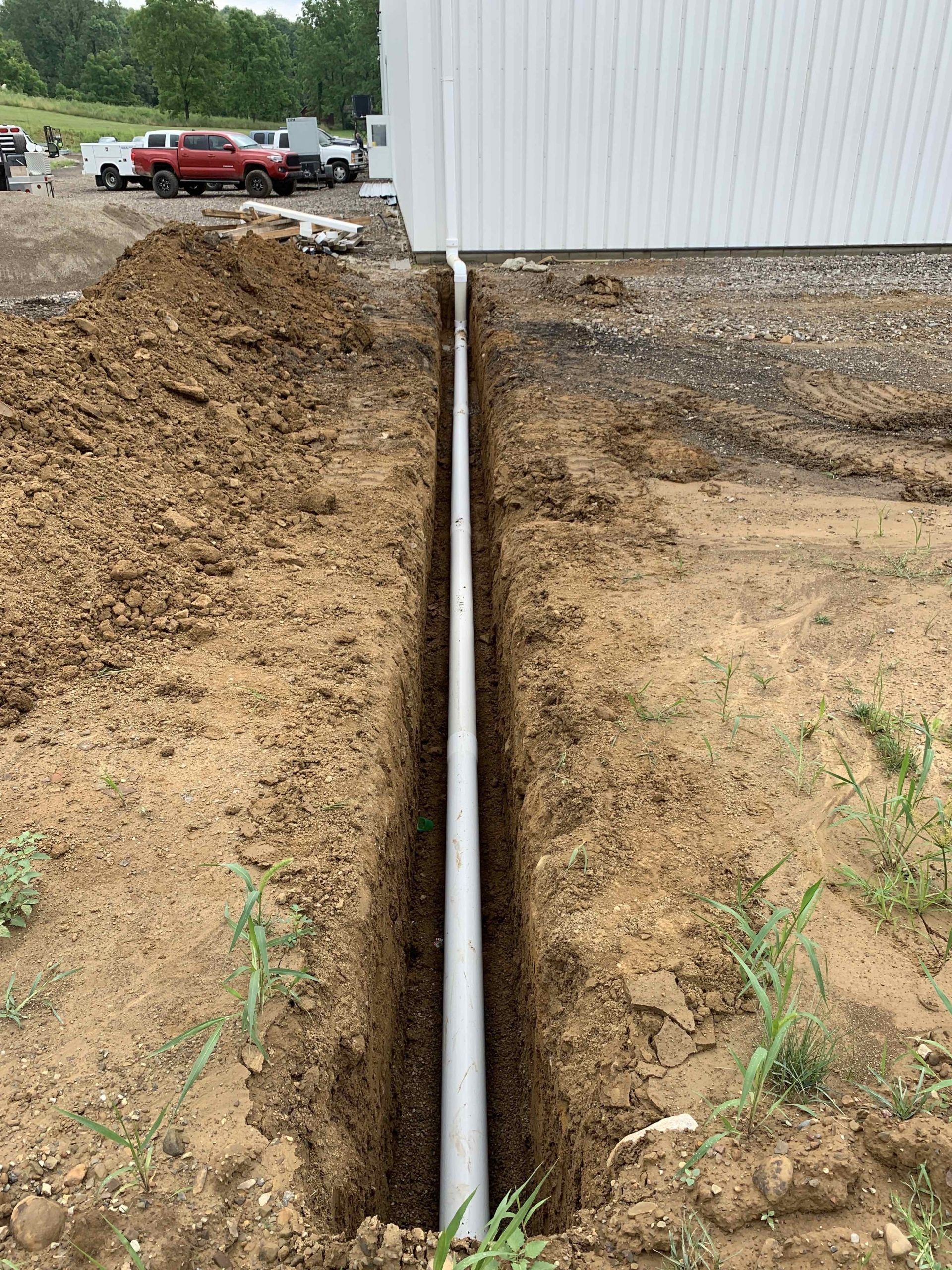 A pipe is being installed in the dirt next to a building.
