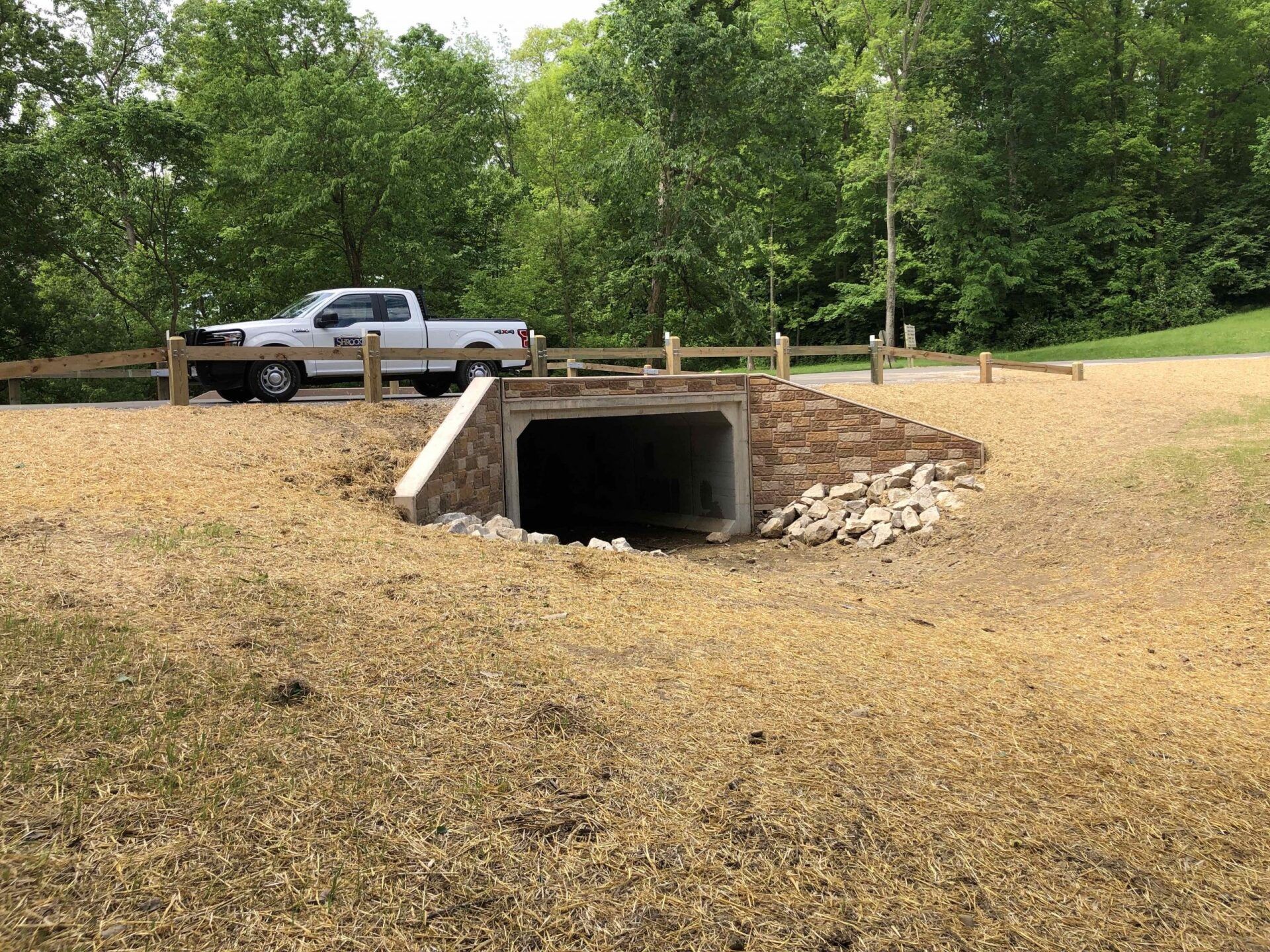 A white truck is parked in a field next to a culvert.