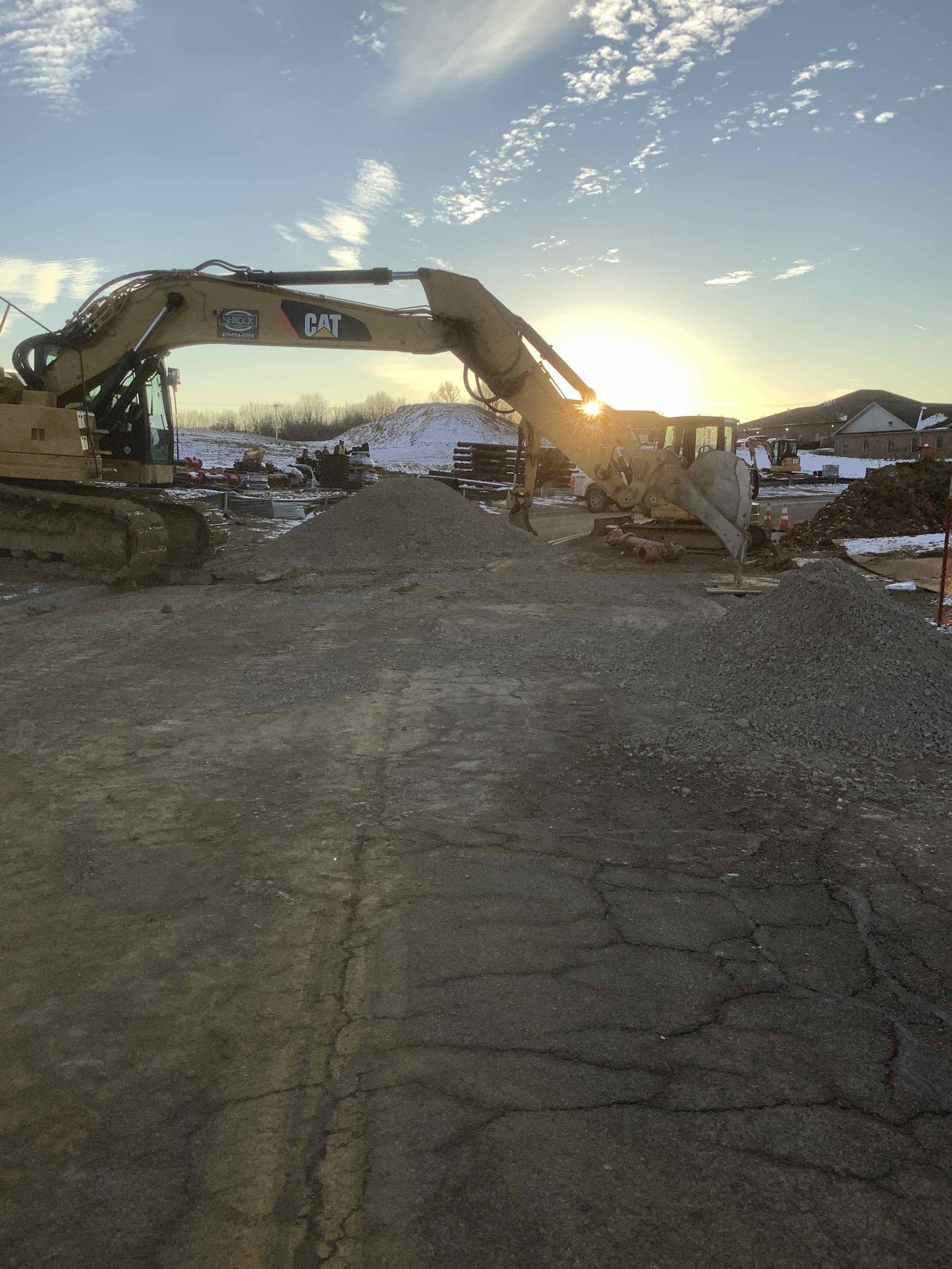 A large excavator is working on a construction site at sunset.