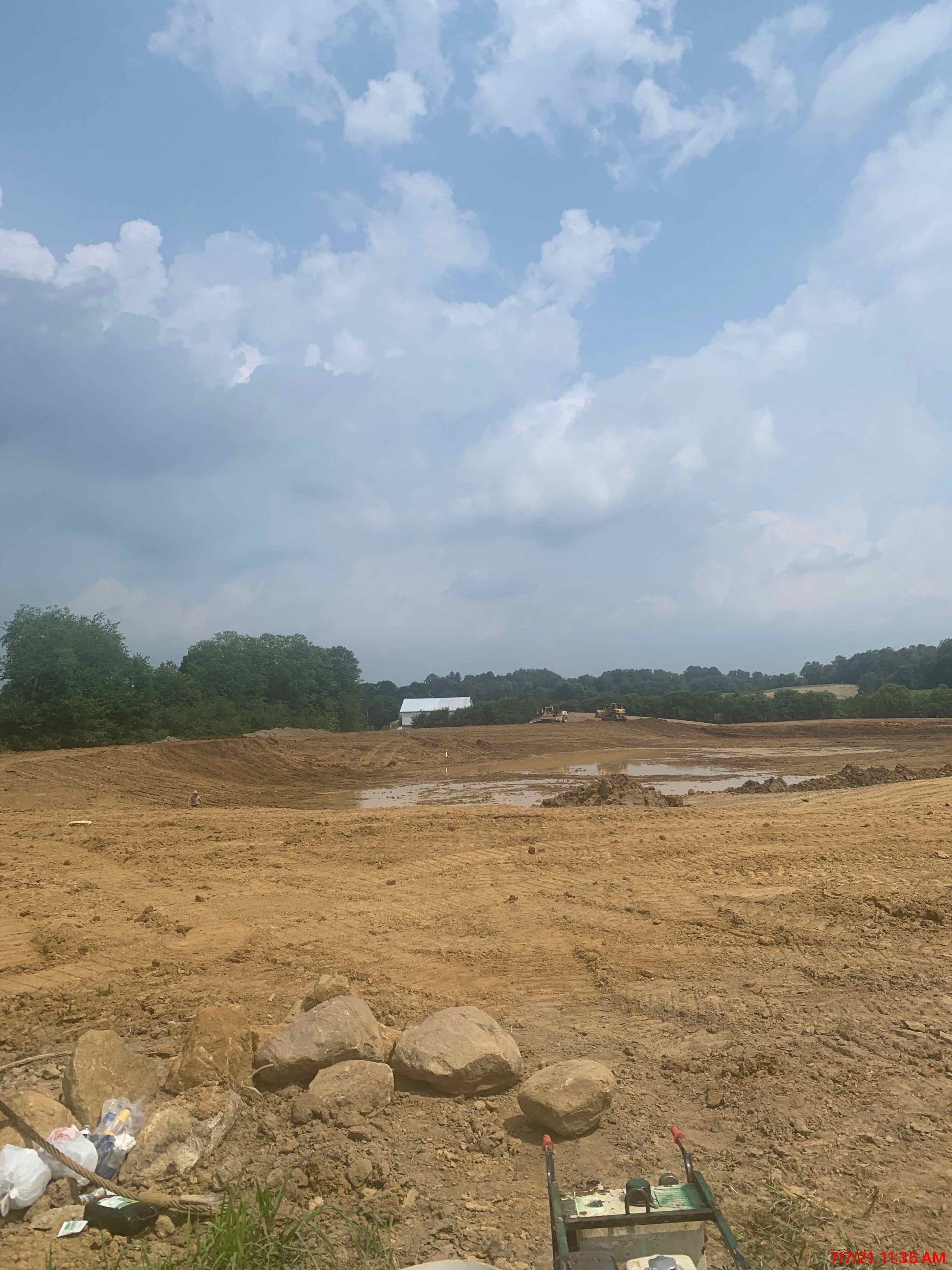 A large dirt field with trees in the background and a blue sky with clouds.