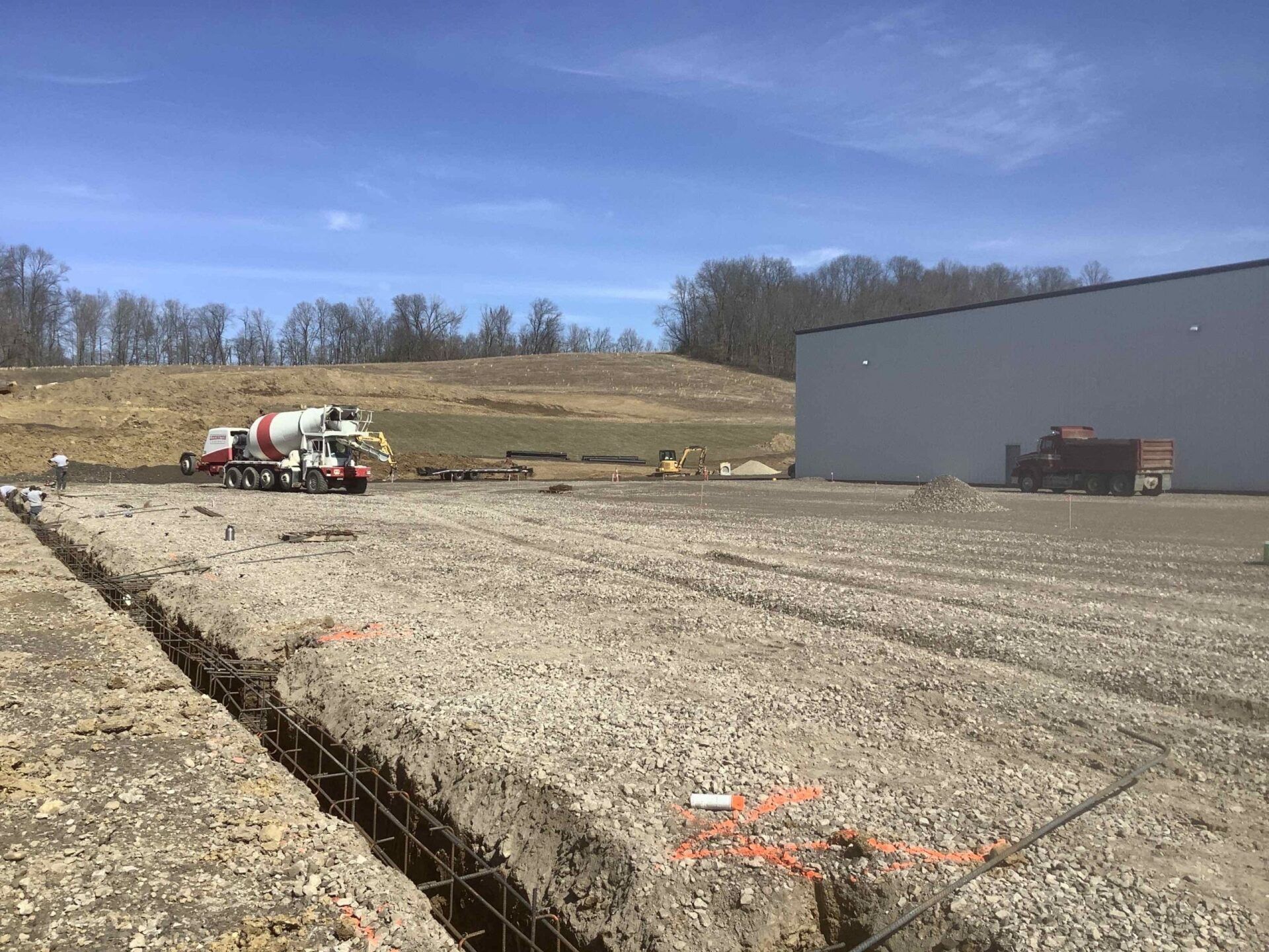 A concrete mixer truck is driving down a dirt road next to a building.