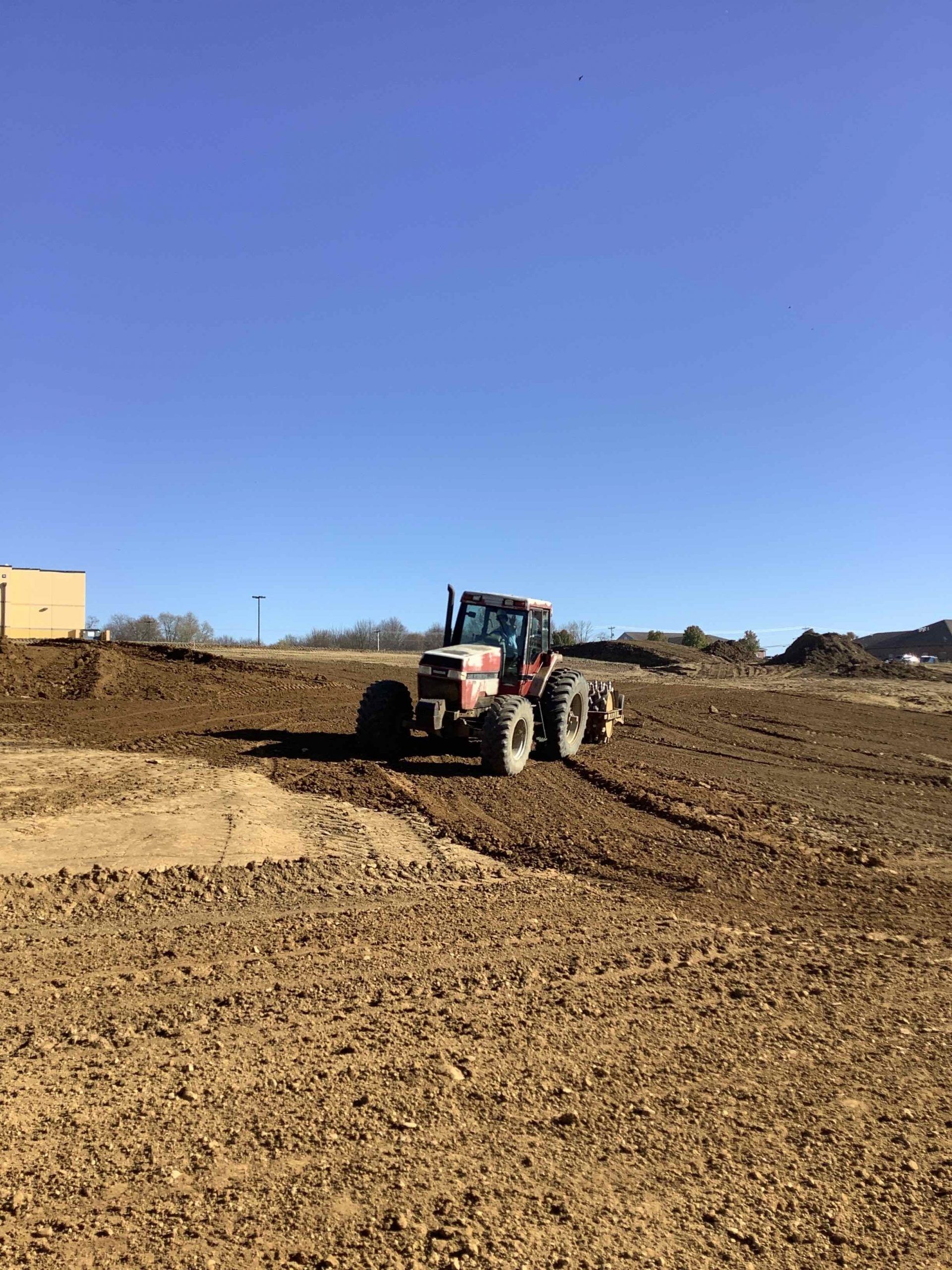 A red and white tractor is driving through a dirt field.