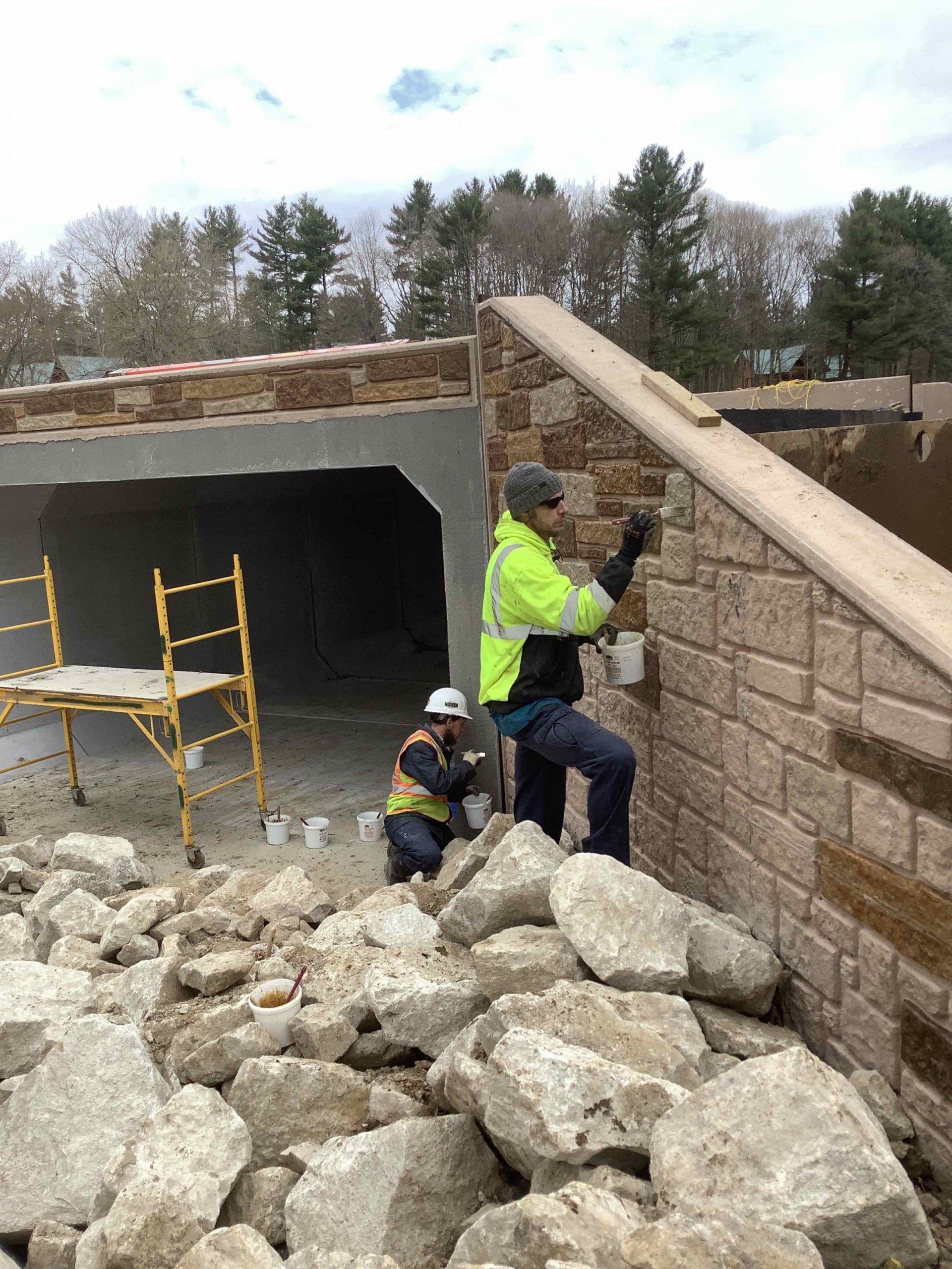 Two construction workers are working on a brick wall.
