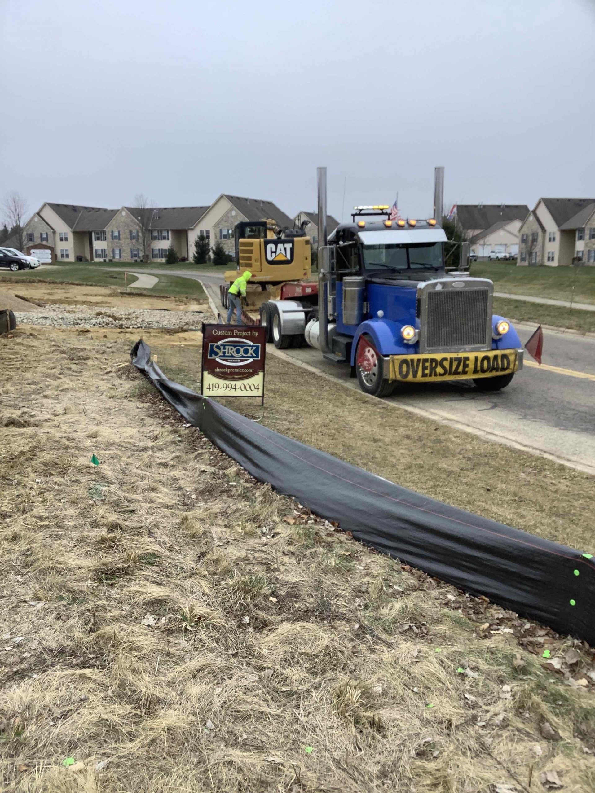 A blue semi truck is driving down a road next to a construction site.