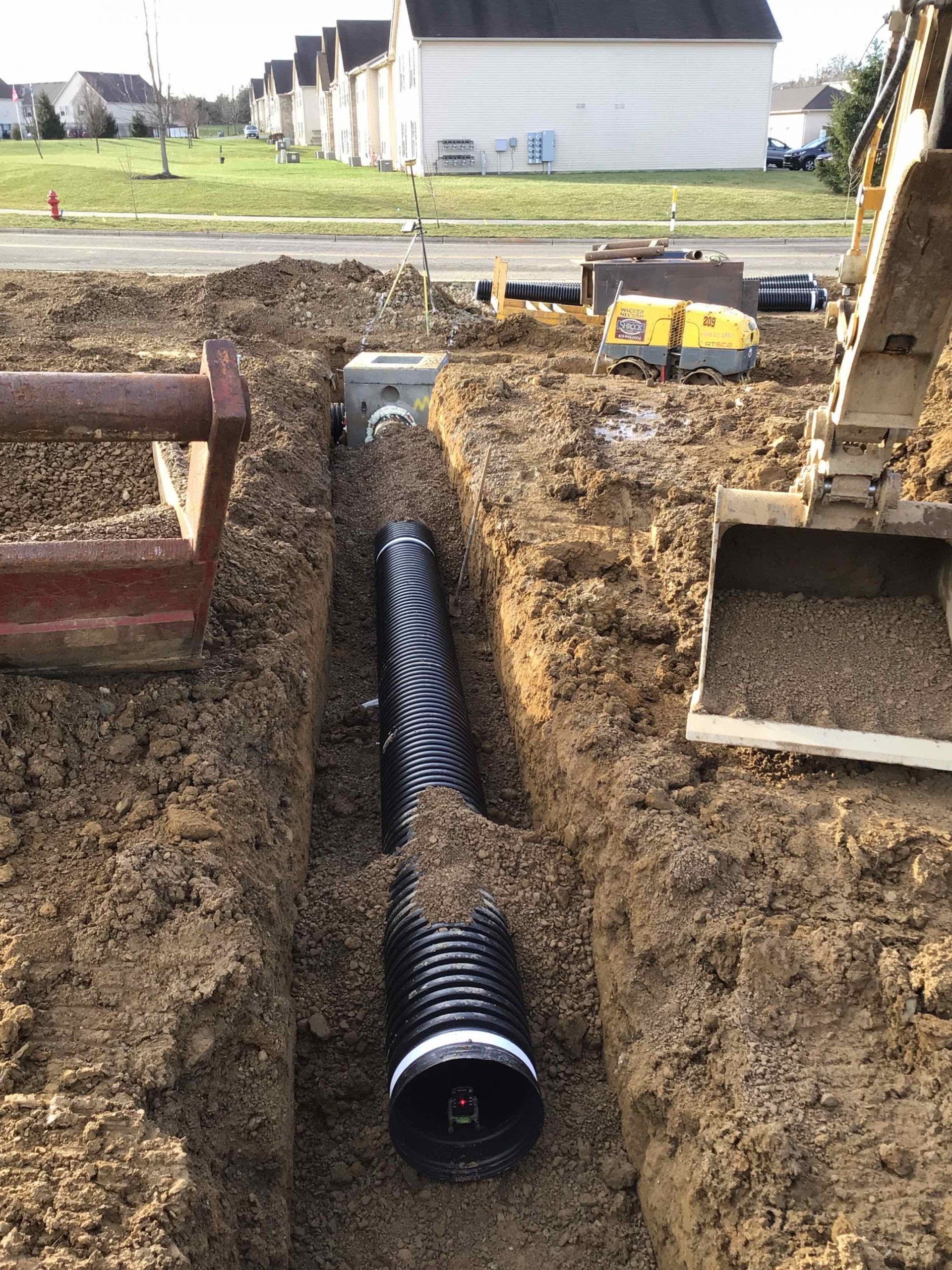 A large black pipe is being installed in the dirt.
