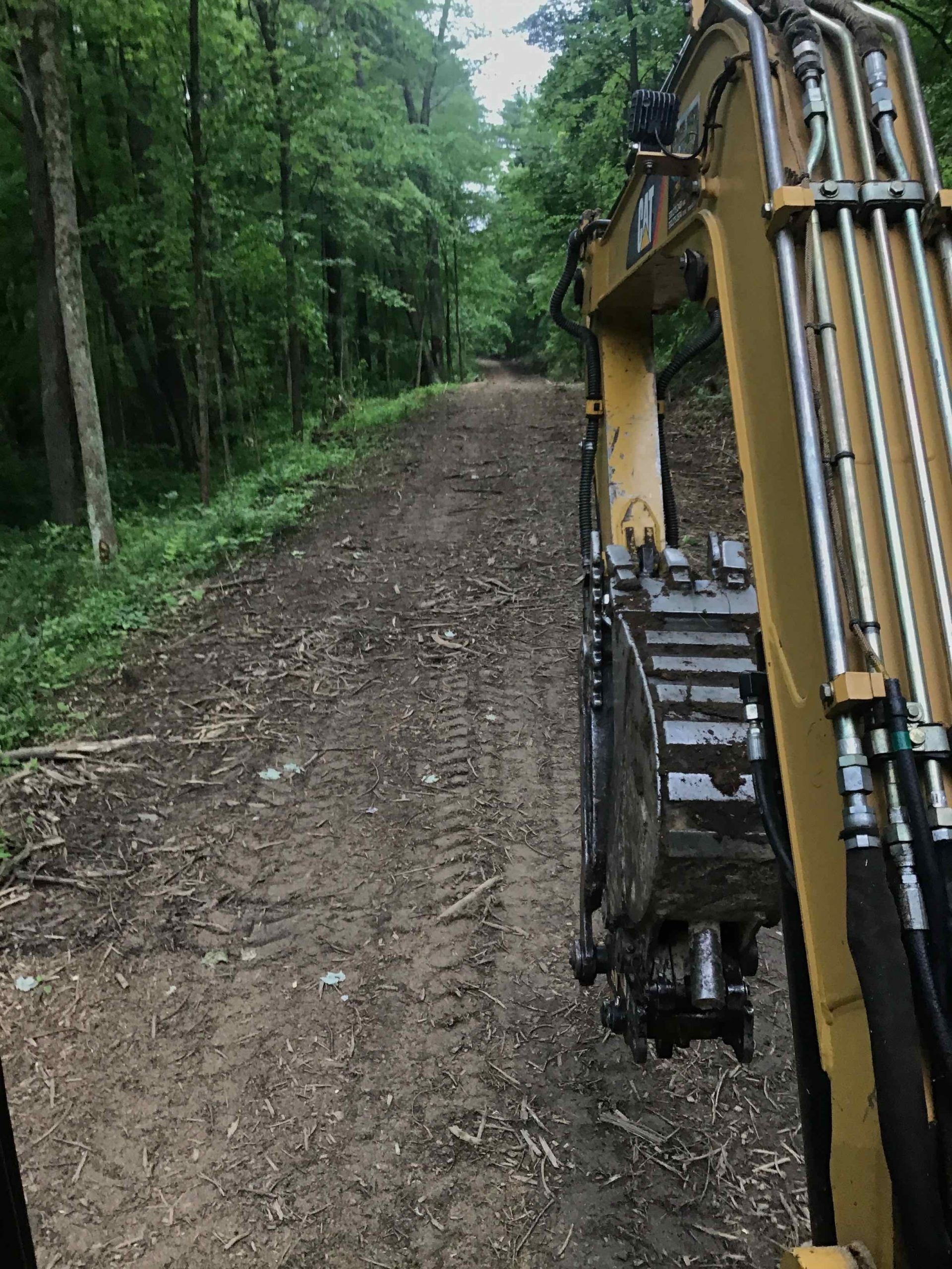 A yellow excavator is driving down a dirt road in the woods.