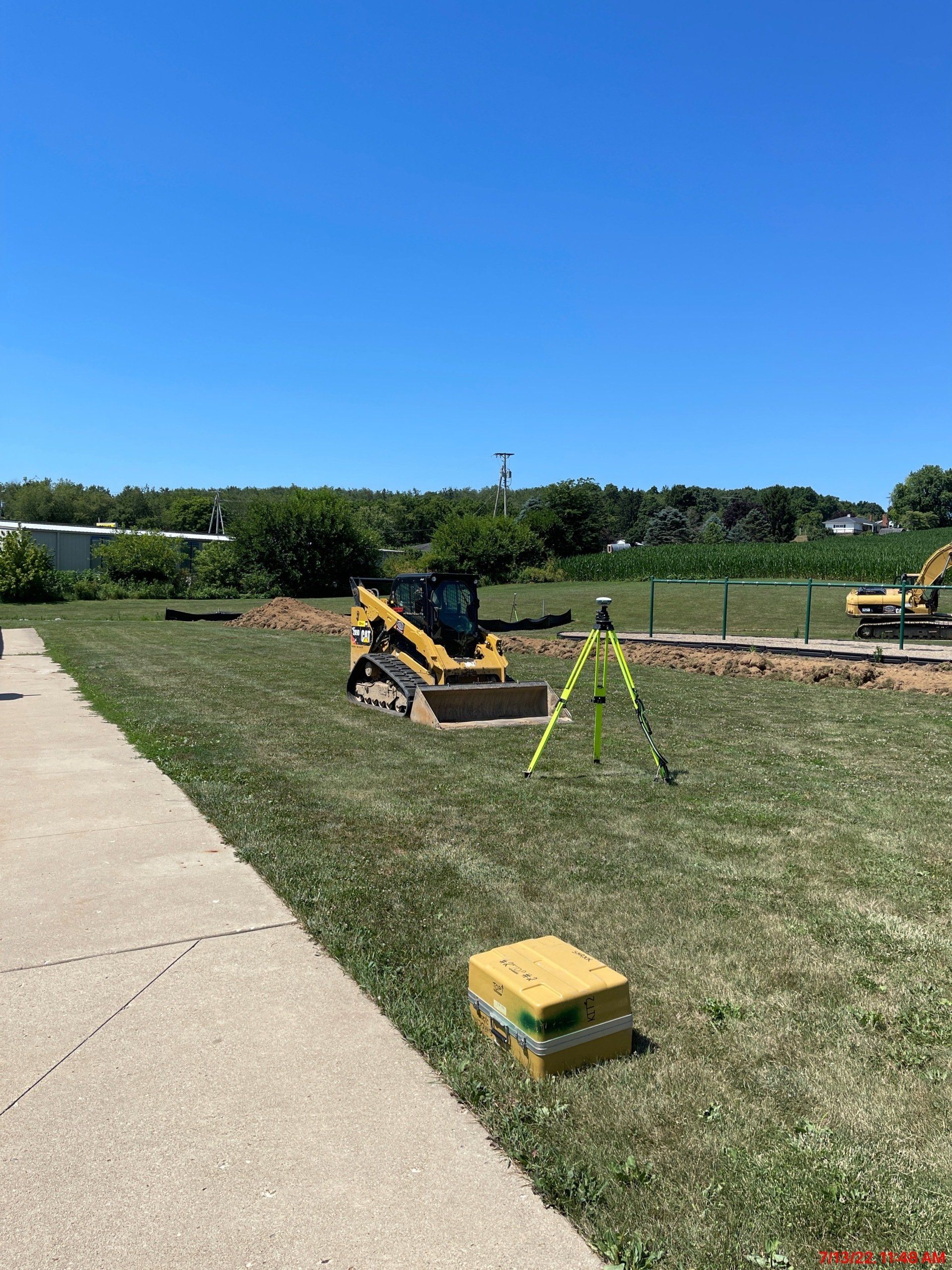 A construction site with a bulldozer and a tripod in the grass.