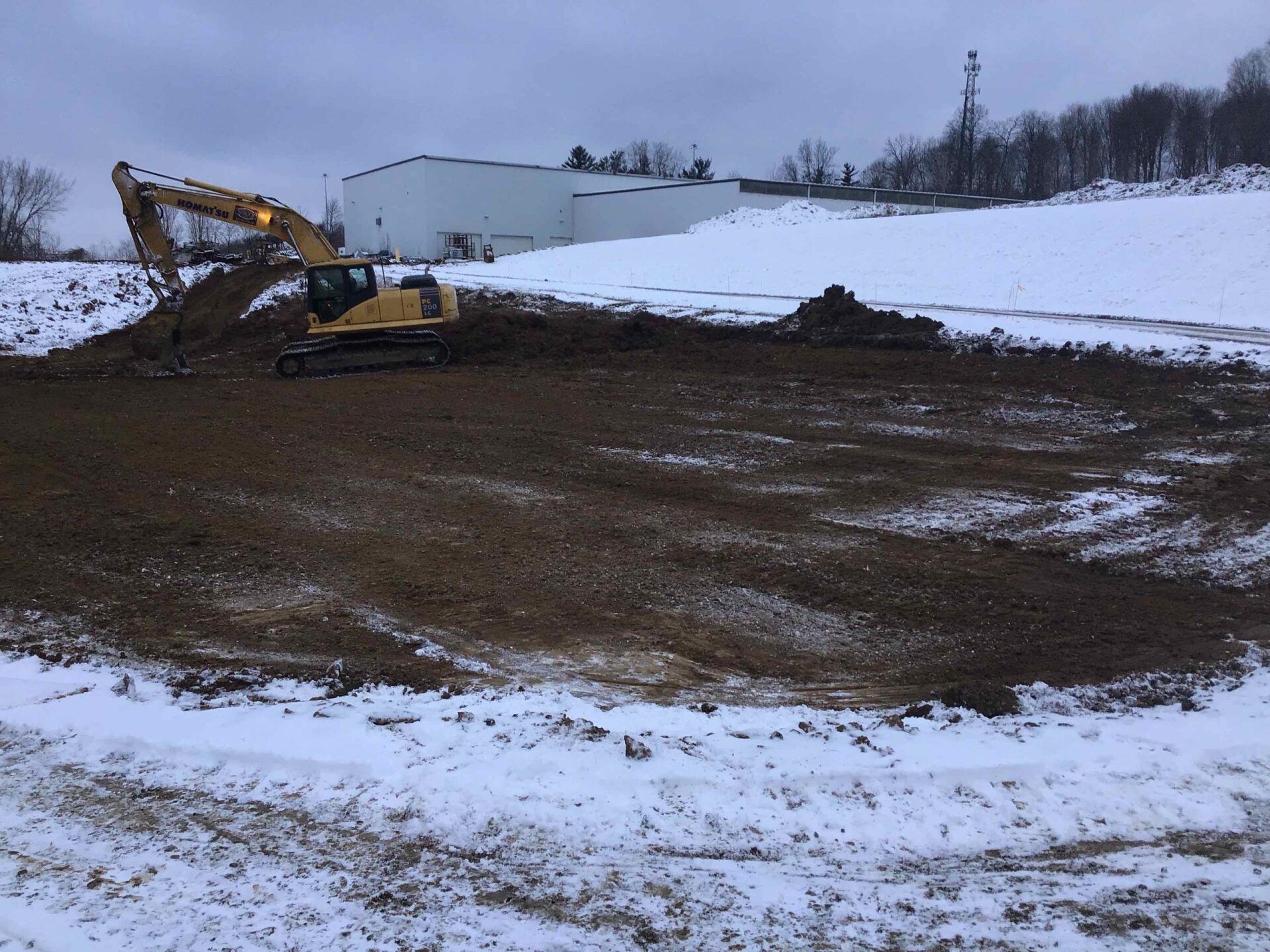 A yellow excavator is moving dirt in a snowy field