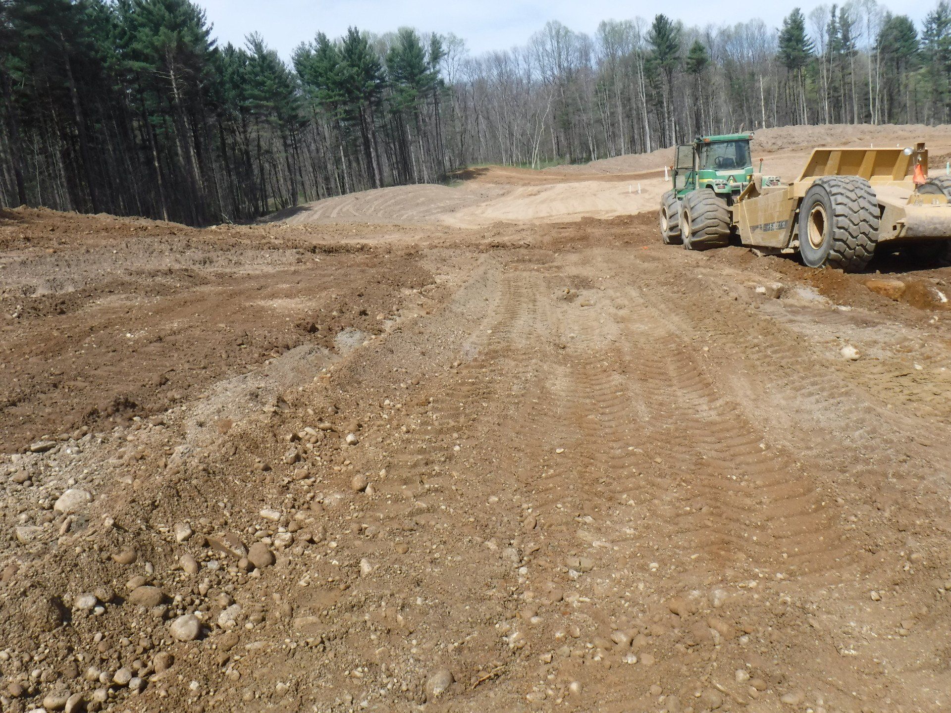 A tractor is driving through a dirt field with trees in the background