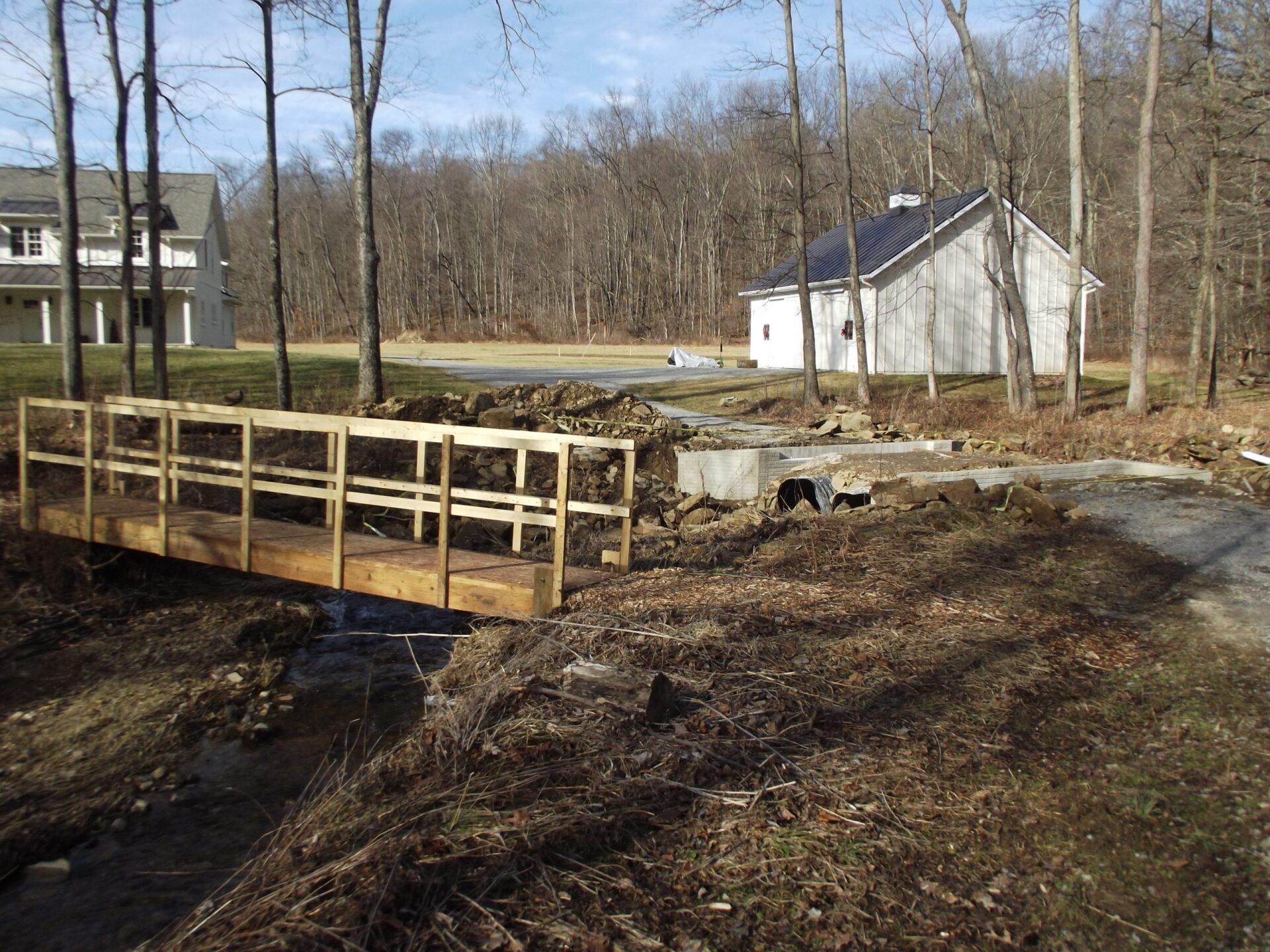 A wooden bridge over a stream with a house in the background