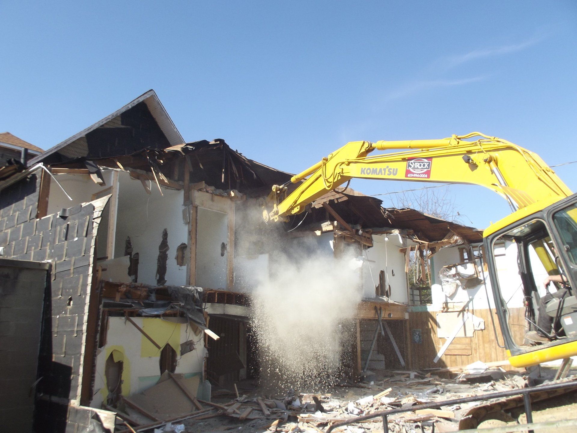 A large yellow excavator is demolishing a building