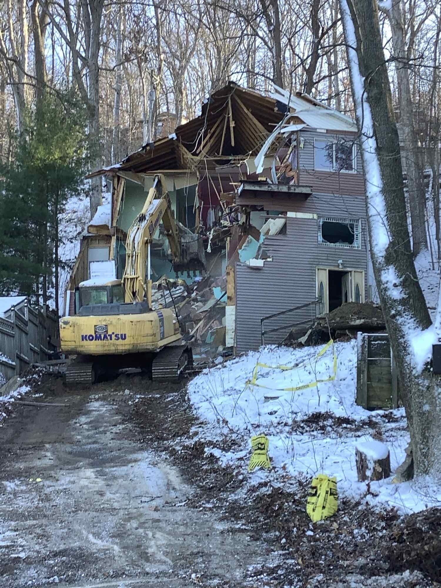 An excavator is demolishing a house in the woods.