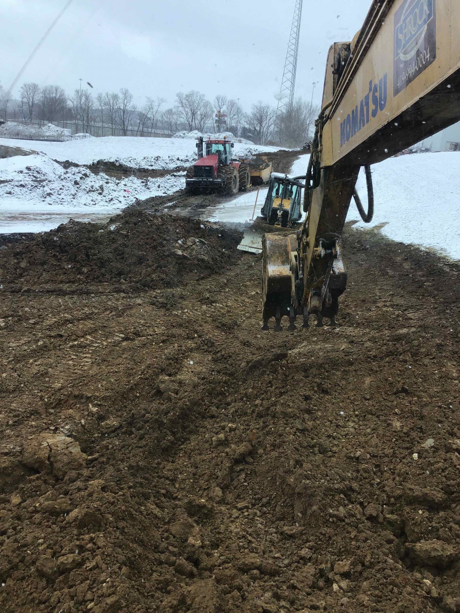 A large excavator is digging a hole in the dirt in a snowy field.