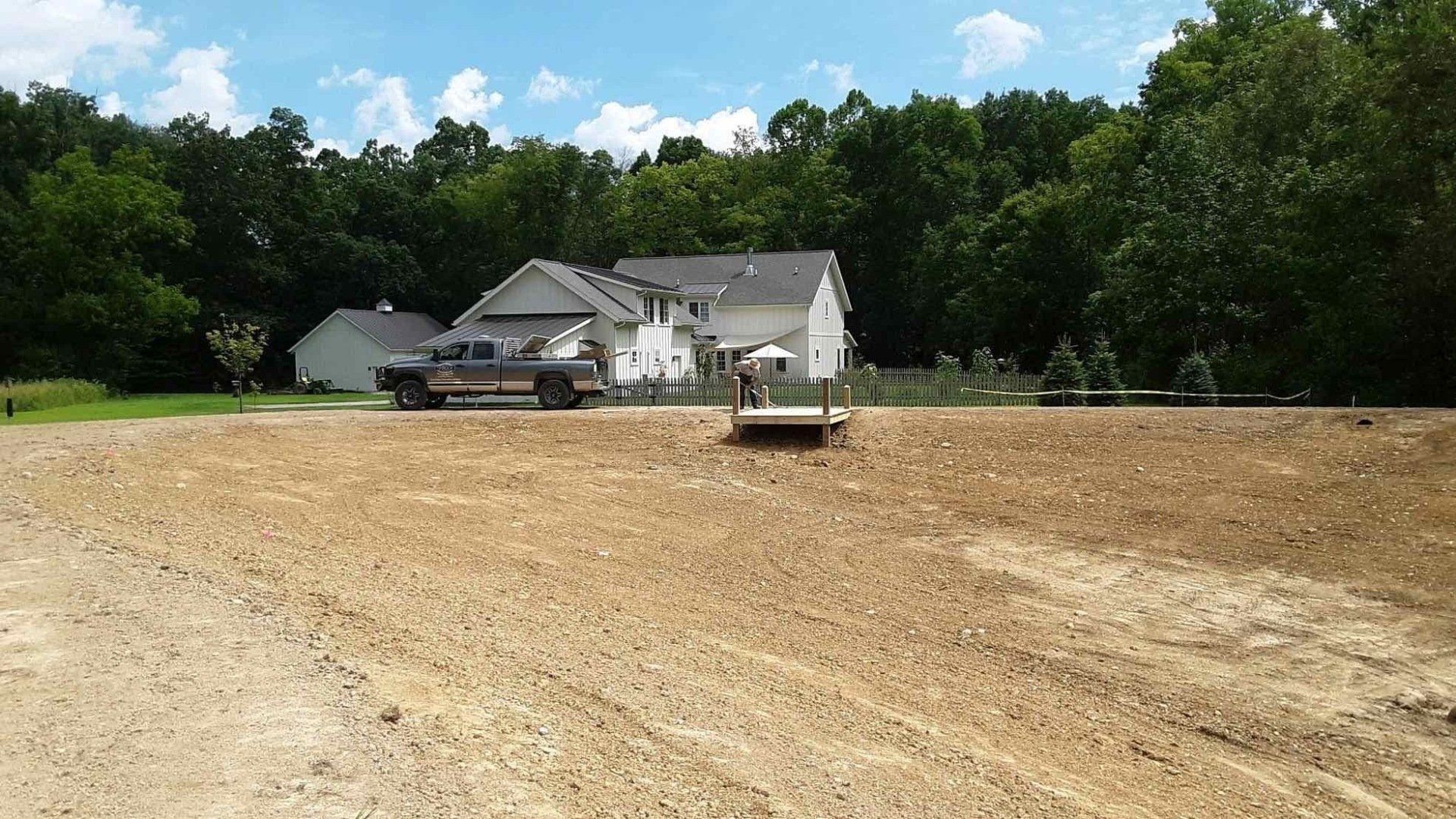 A truck is parked in a dirt field in front of a house
