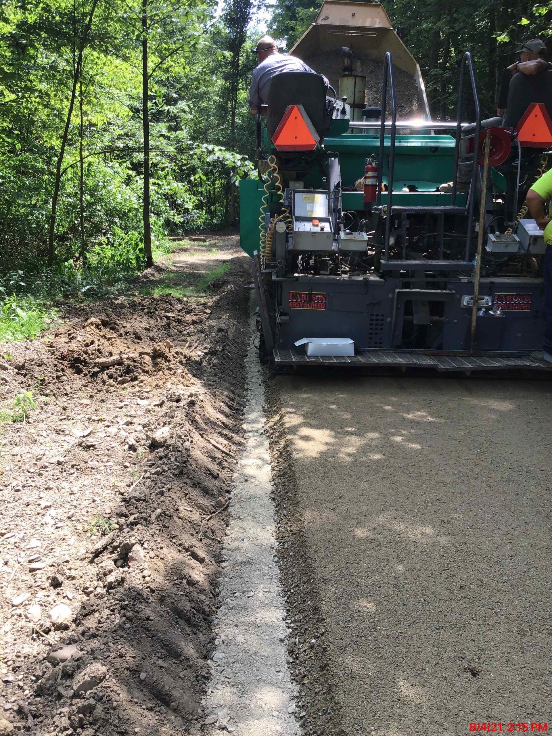 A machine is laying gravel on a dirt road.