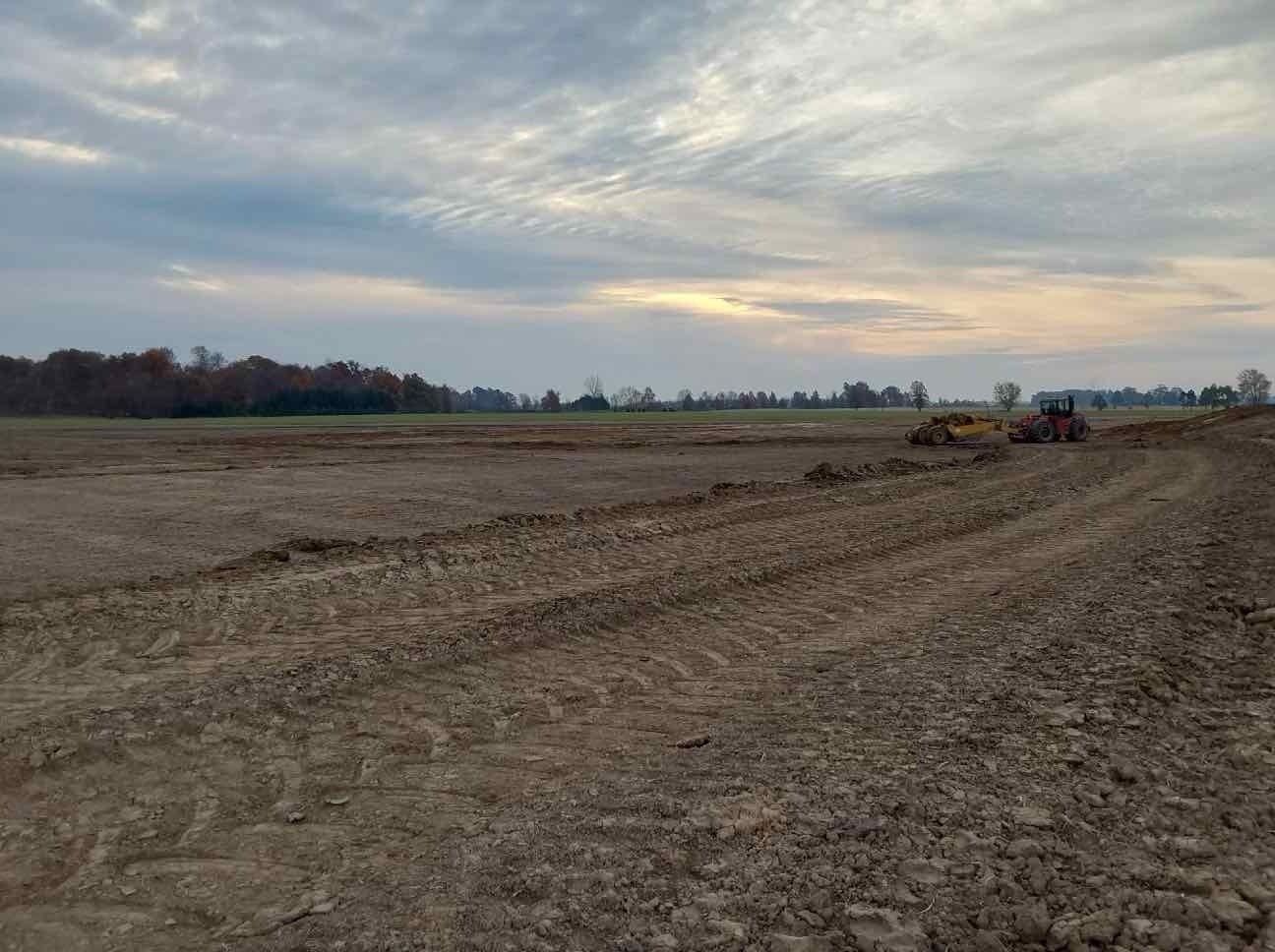 A tractor is plowing a dirt field with a cloudy sky in the background.