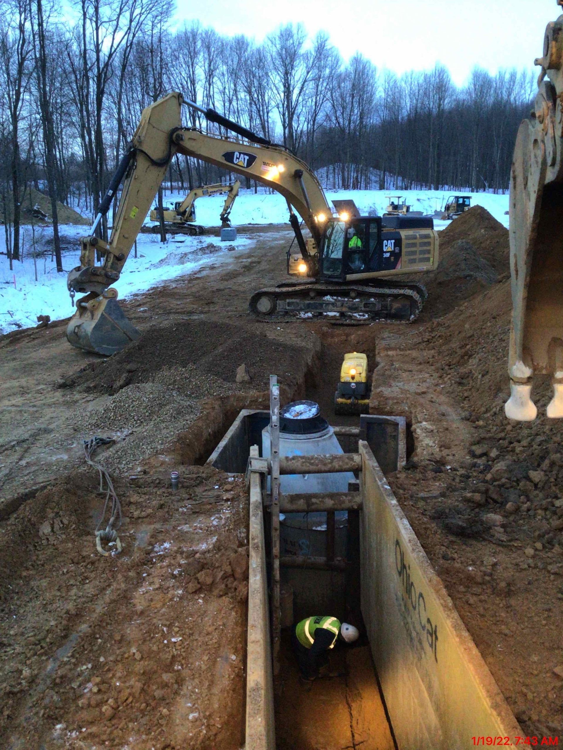 A man is standing in a trench next to a large excavator.
