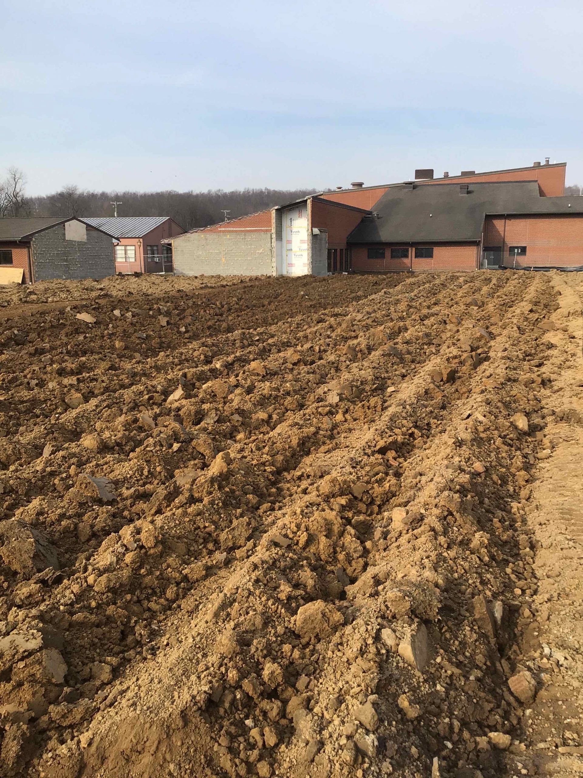 A large field of dirt with a house in the background.