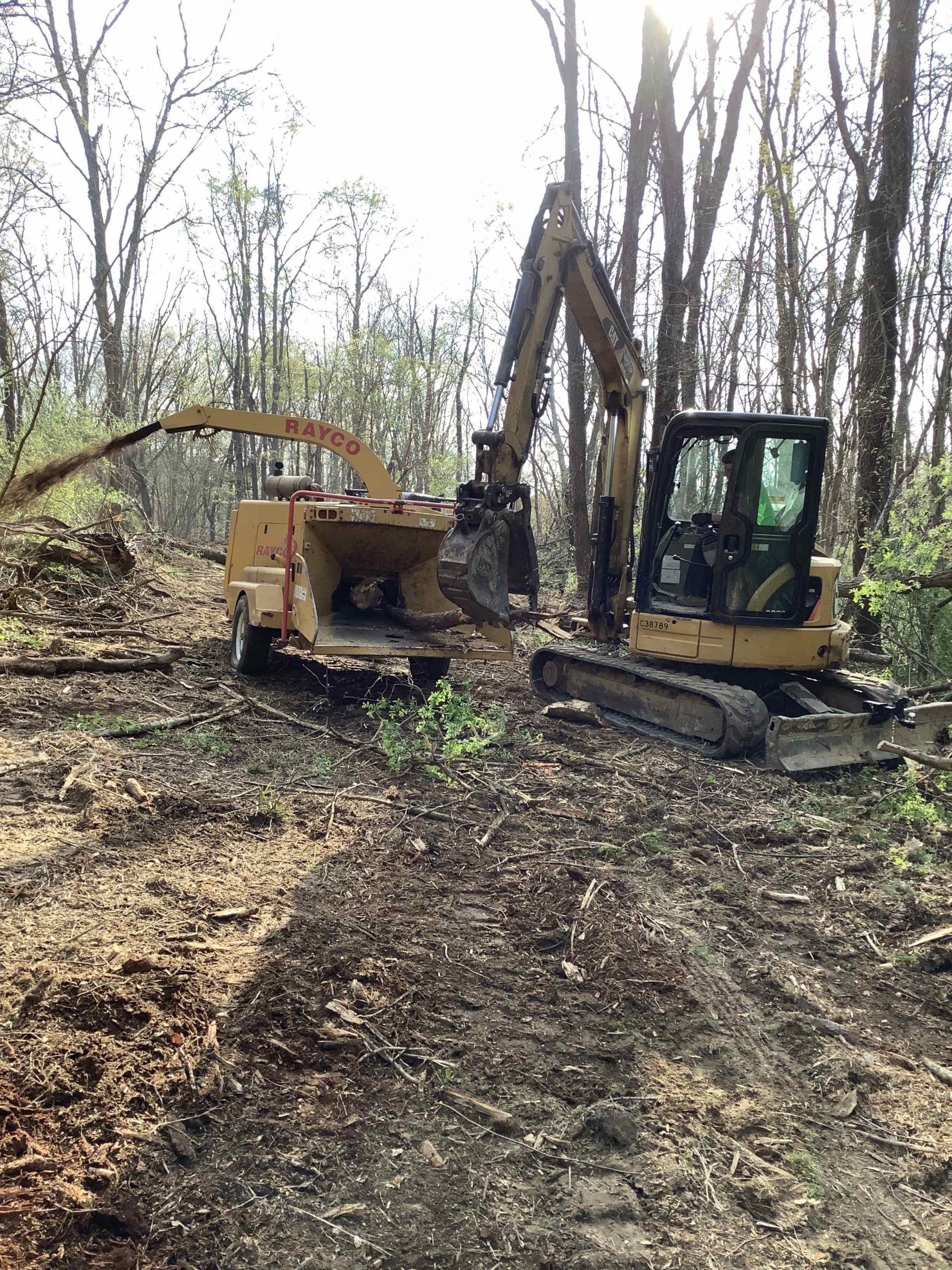 A bulldozer and a wood chipper are working in the woods.
