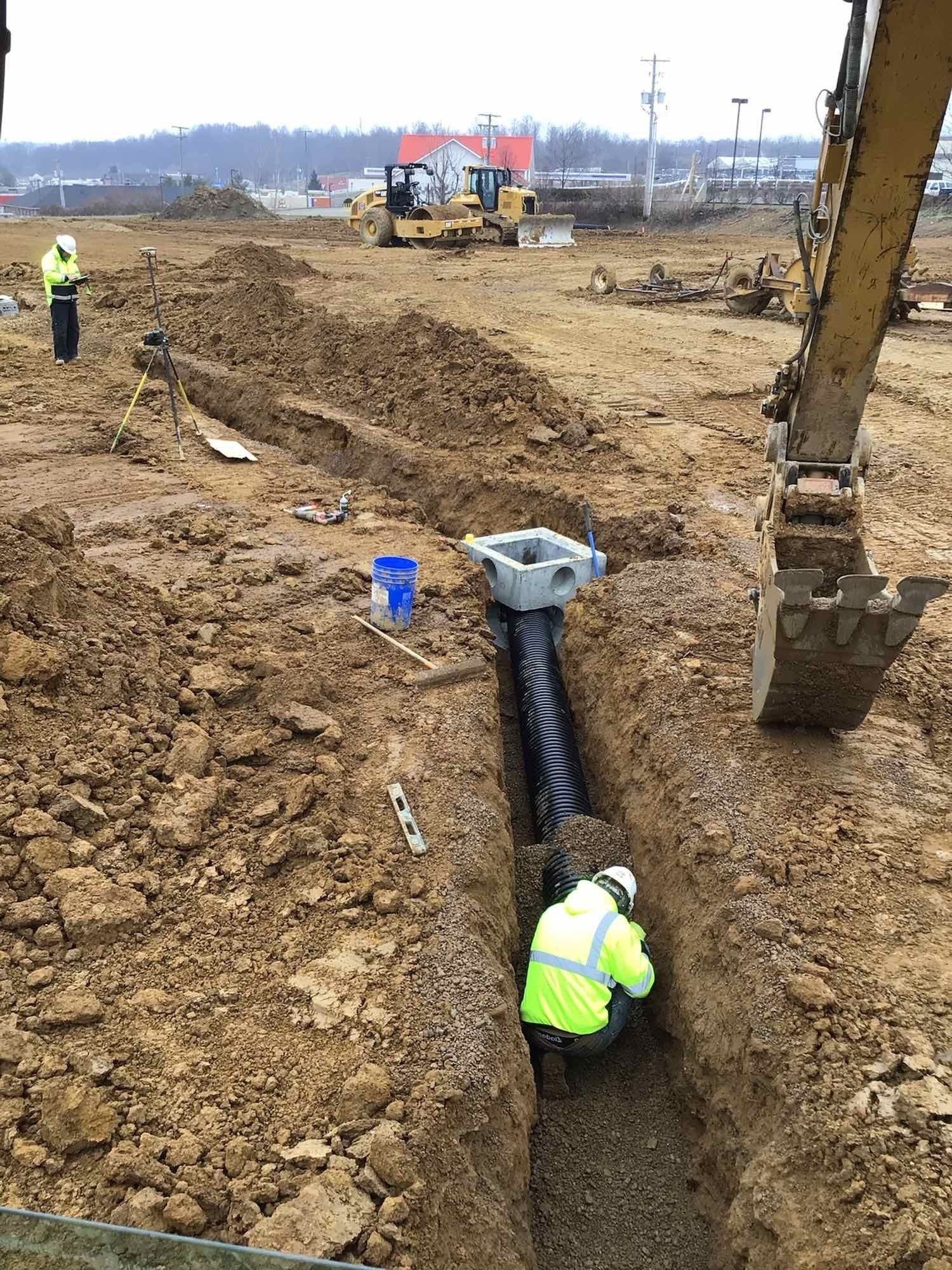 A man is working on a pipe in the dirt in a construction site.