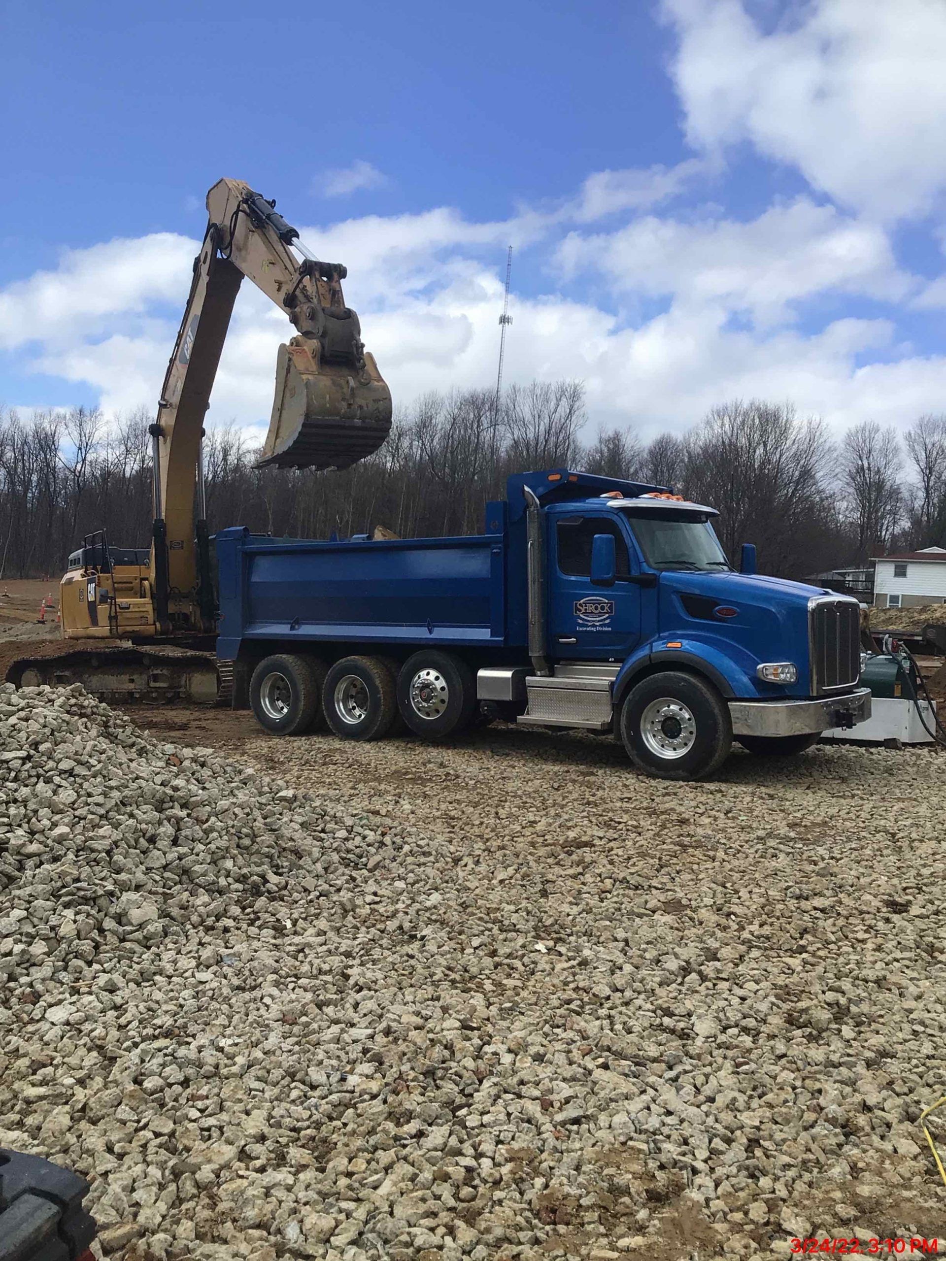 A blue dump truck is being loaded with gravel by an excavator.