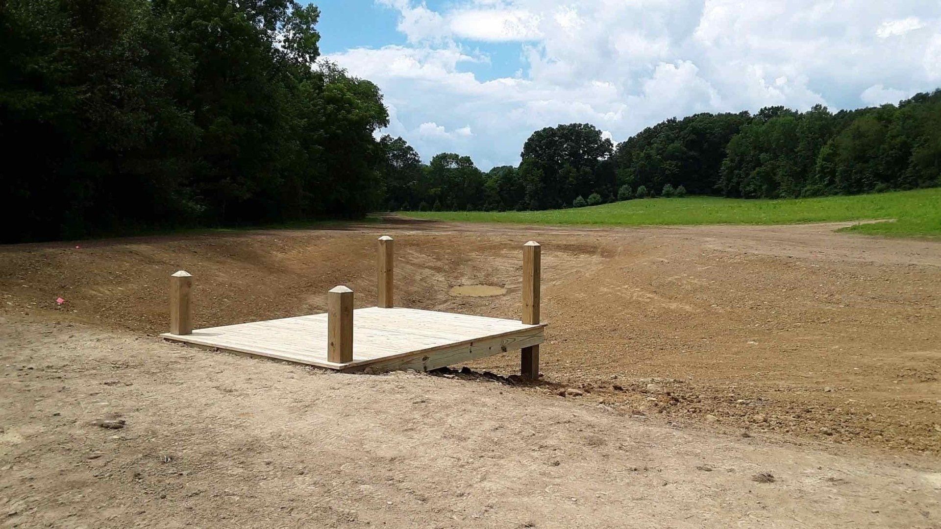 A wooden platform is sitting in the middle of a dirt field.