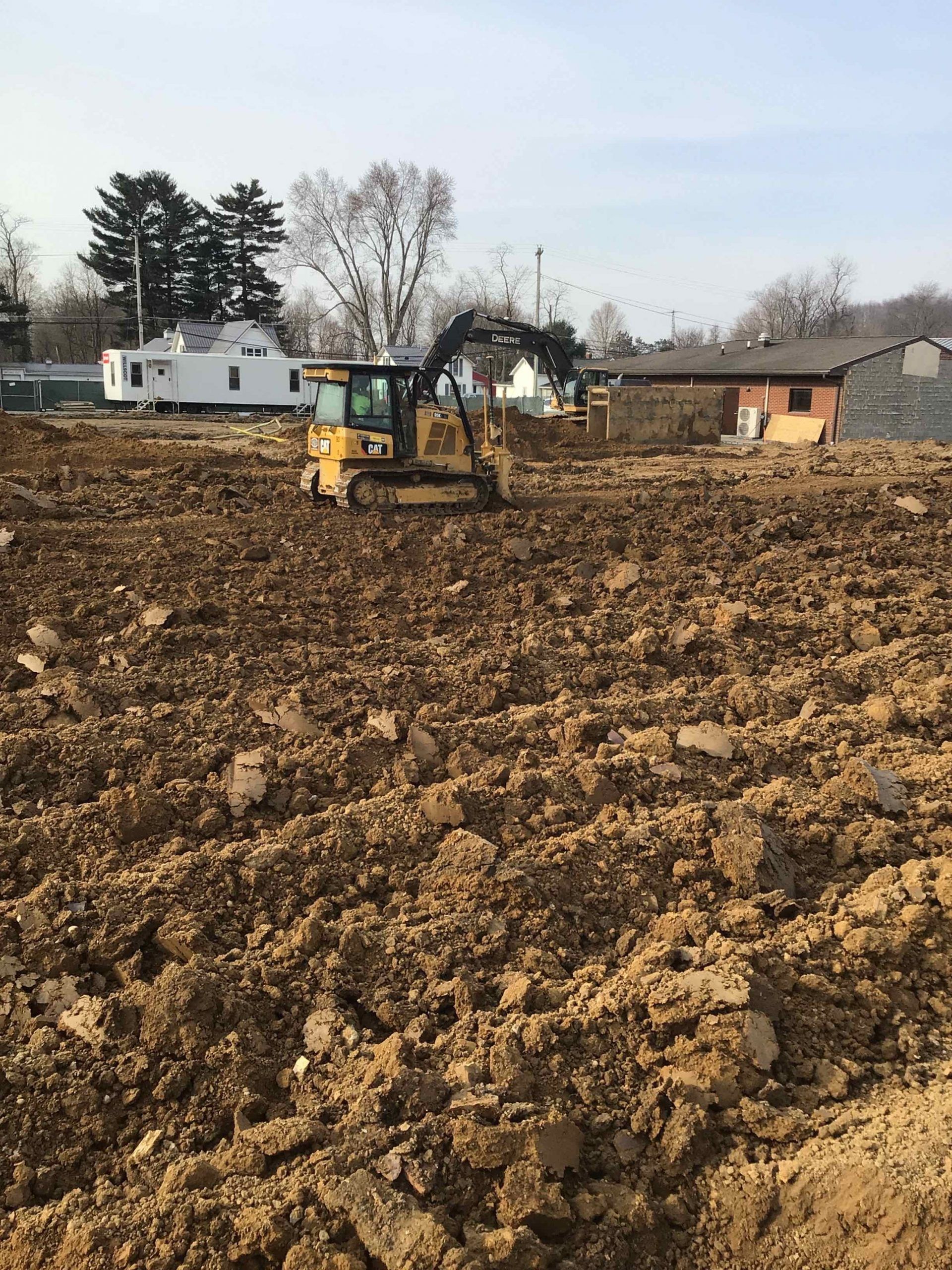 A bulldozer is moving dirt in a field with a house in the background.