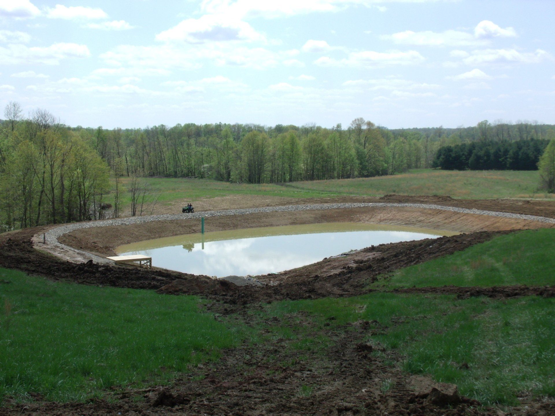 A small pond in the middle of a field with trees in the background