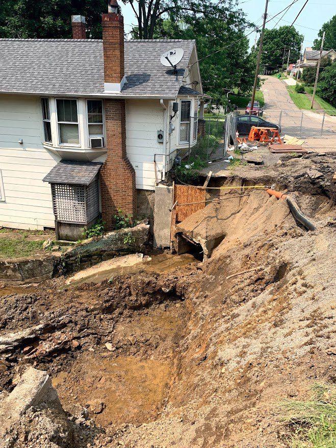A house is sitting on top of a dirt hill next to a road.