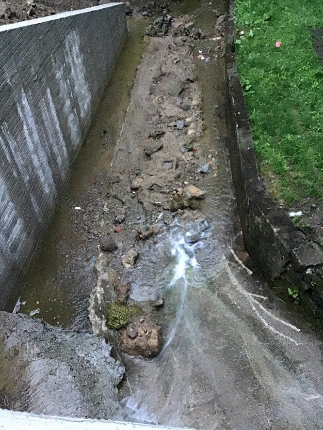 A muddy stream running through a brick wall next to a grassy area.