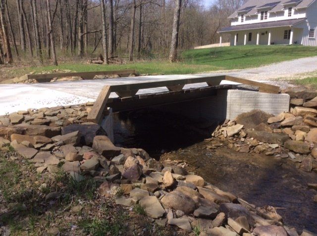 A bridge over a stream with a house in the background