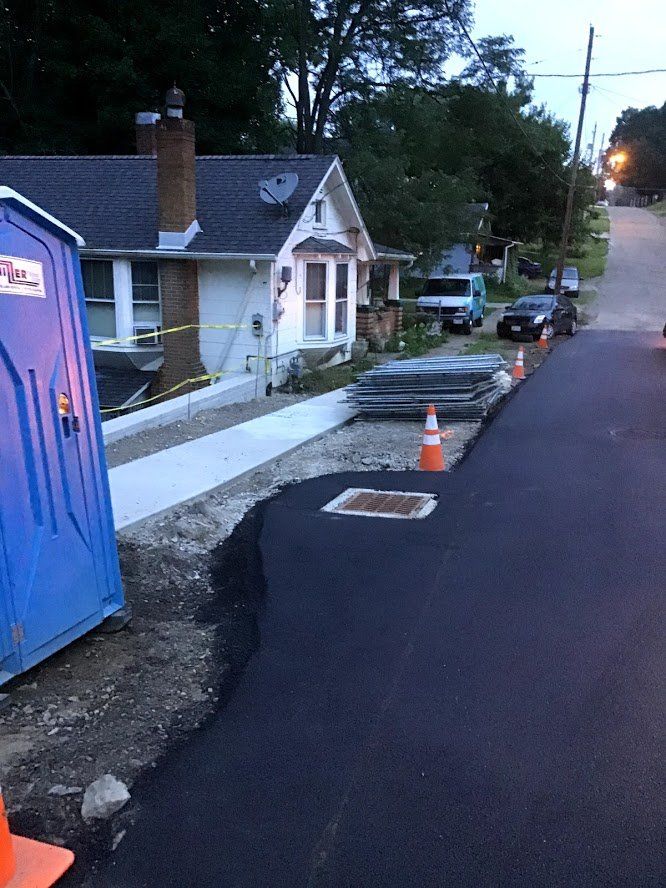 A blue portable toilet is sitting on the side of a street next to a house.