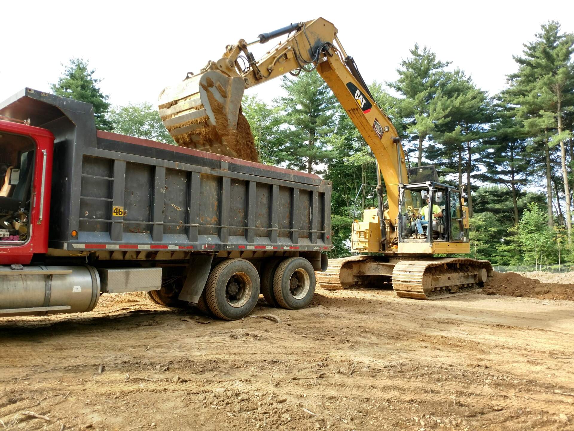 A dump truck is being loaded with dirt by an excavator.