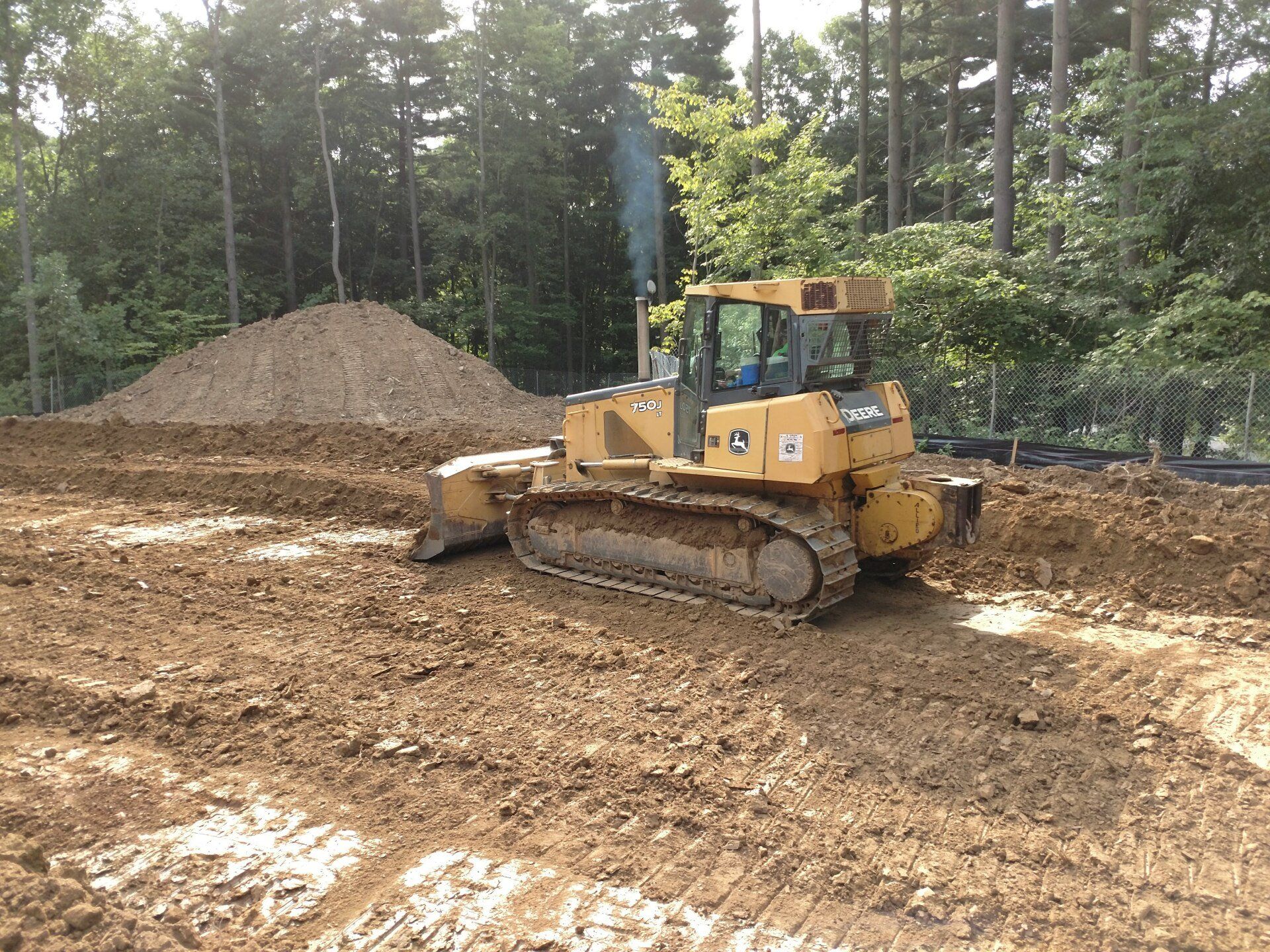 A bulldozer is moving dirt in a field with trees in the background