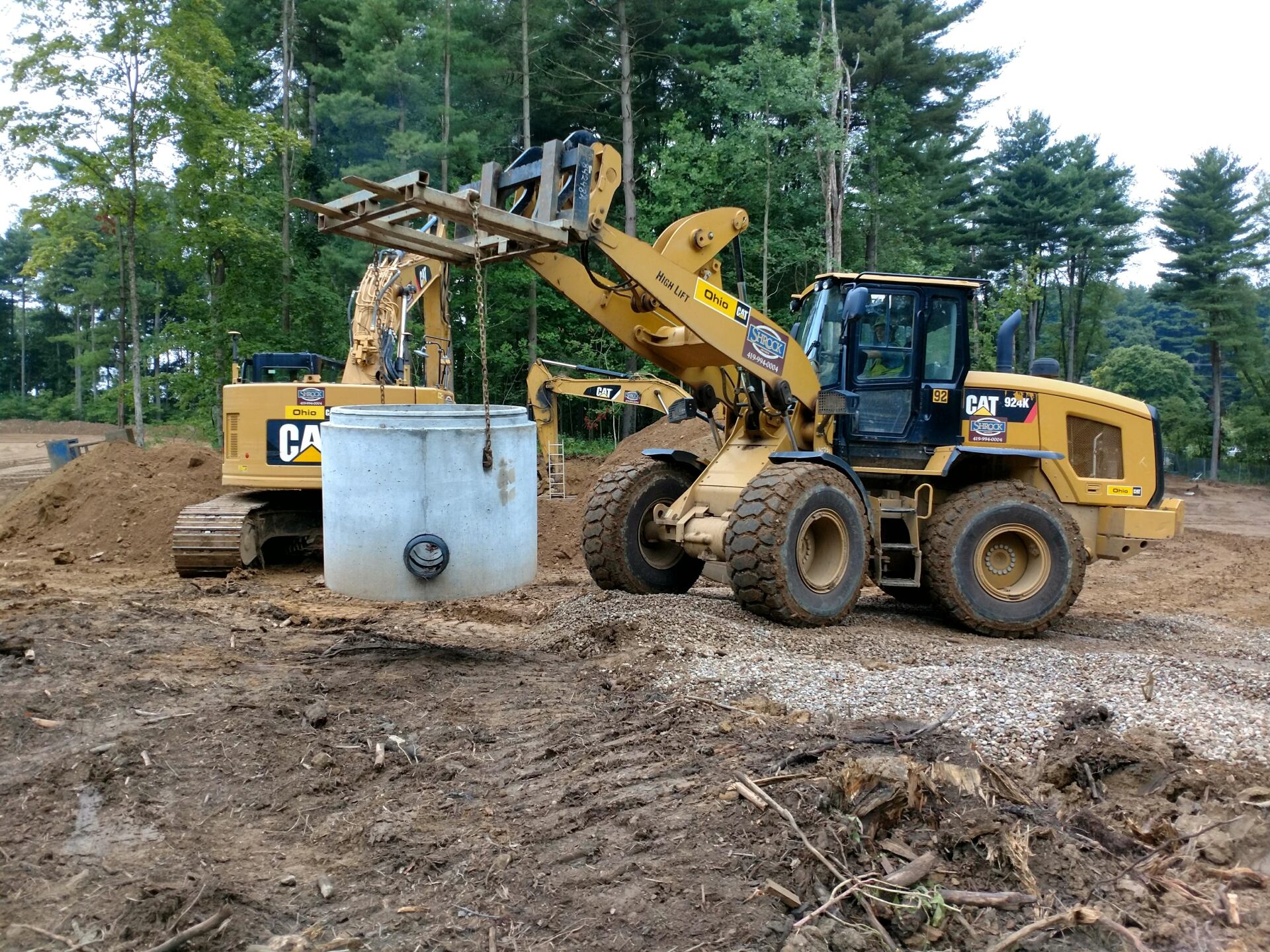 A bulldozer is lifting a concrete cylinder in a dirt field.