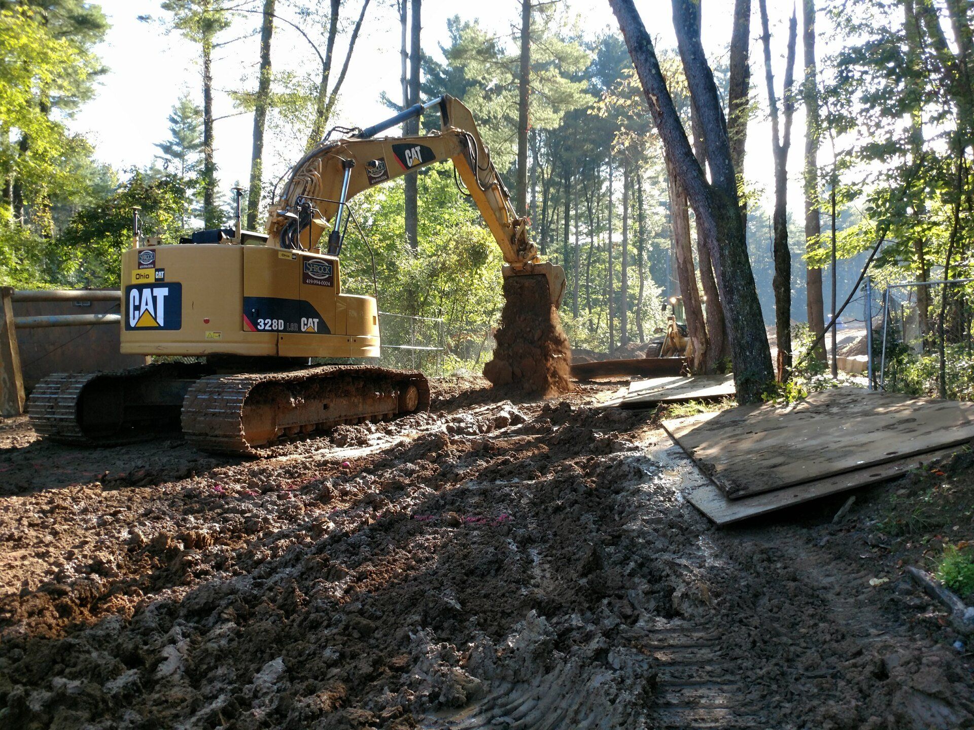 A cat excavator is digging in the dirt in the woods