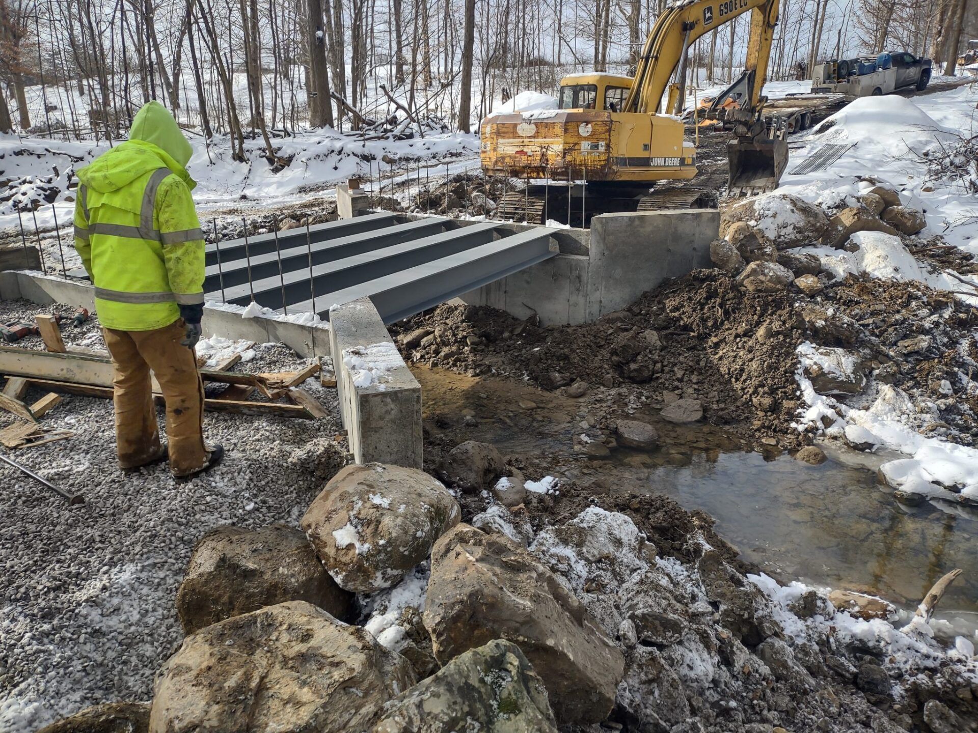 A man in a yellow jacket is standing next to a yellow excavator.