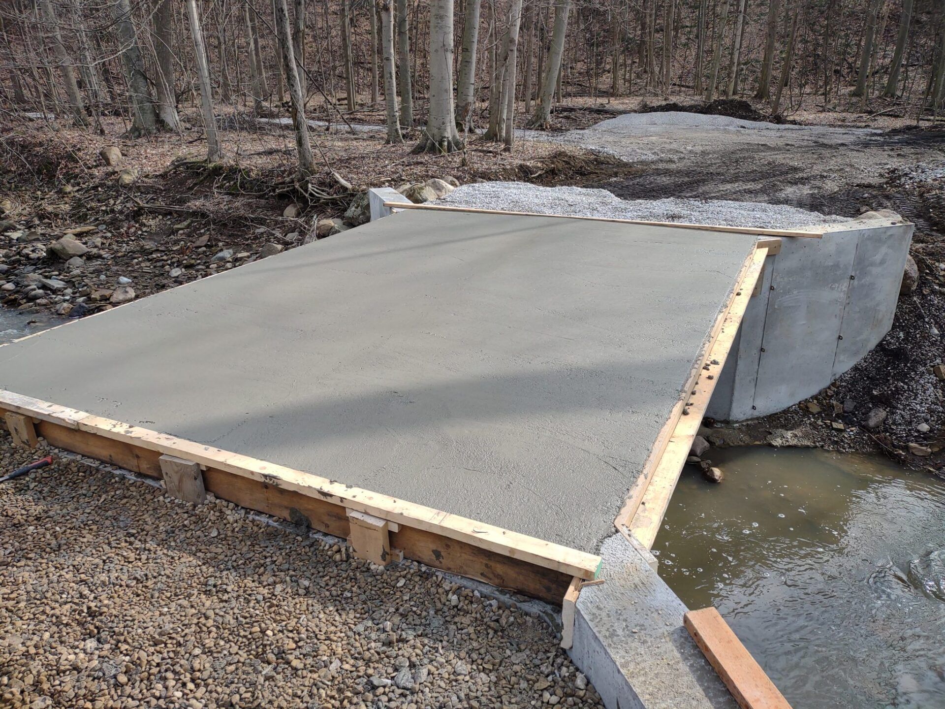 A concrete bridge is being built over a stream in the woods