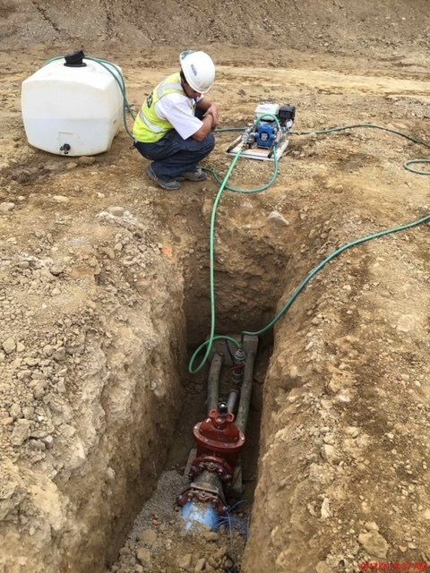 A man is working on a pipe in a trench.