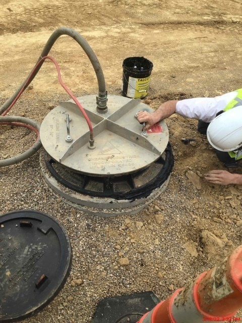 A man is kneeling on the ground next to a manhole cover.