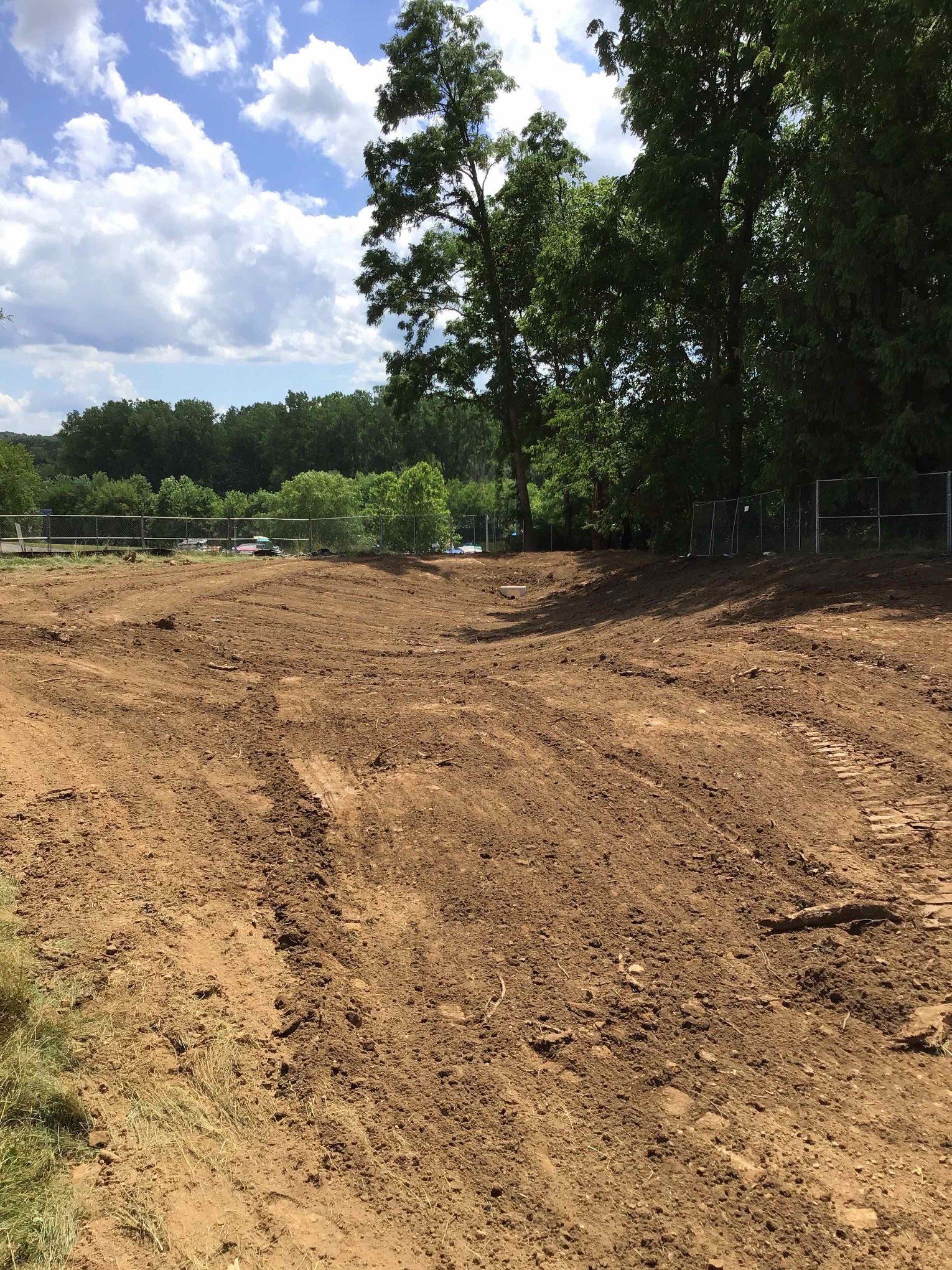 A dirt road going through a field with trees in the background.
