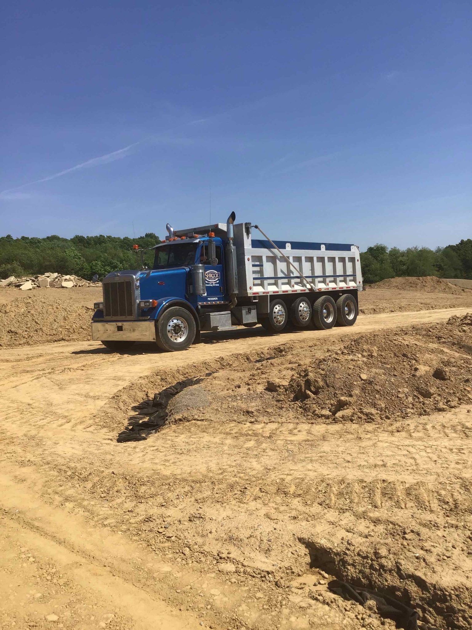 A blue dump truck is driving down a dirt road.