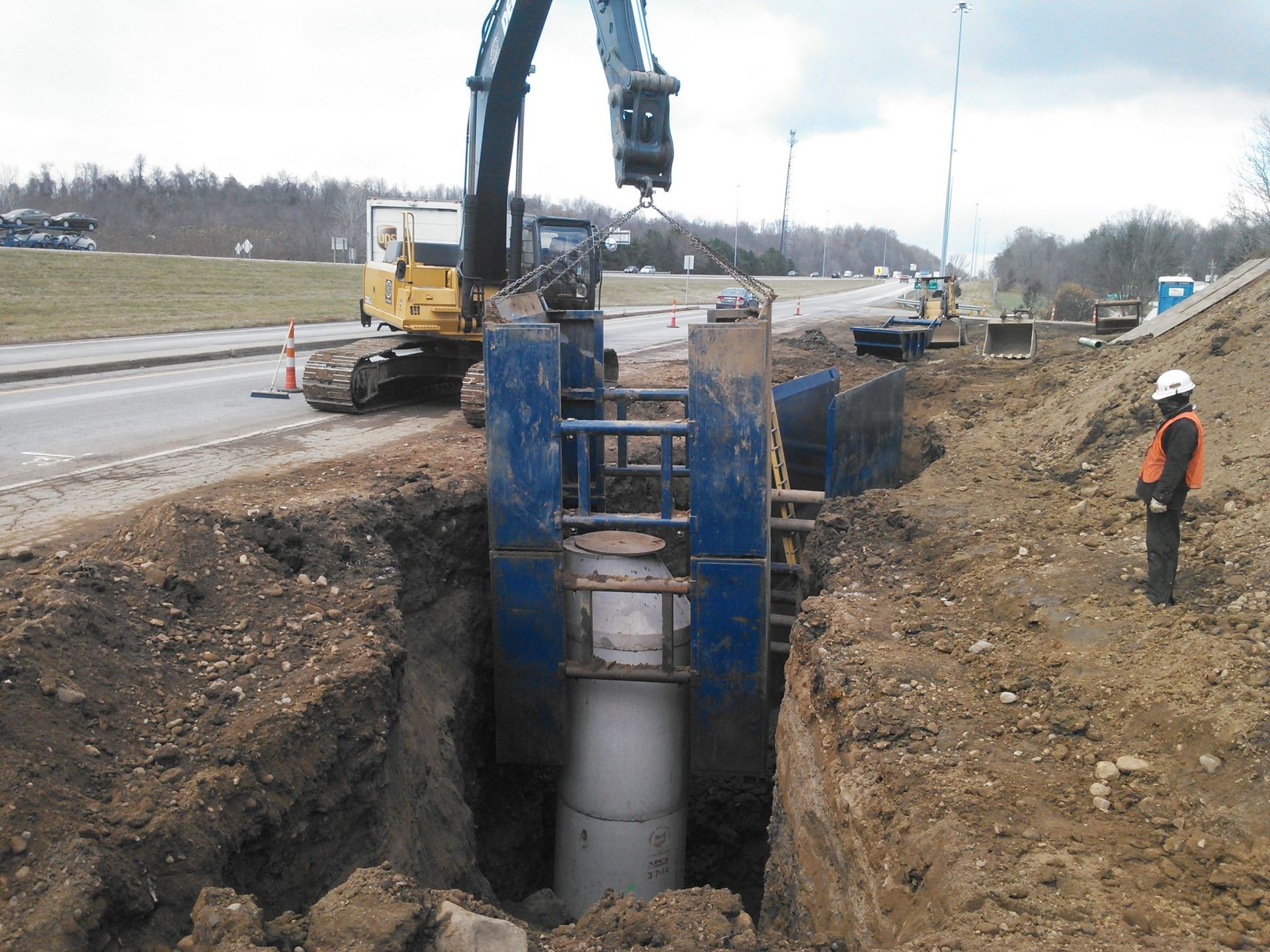 A man in a hard hat stands in the dirt near a construction site