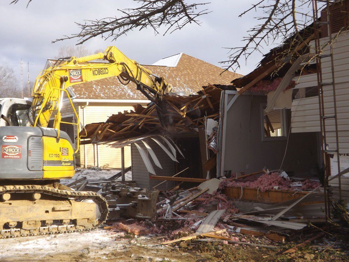 A house is being demolished by a yellow excavator that says komatsu