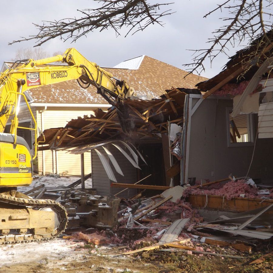 A yellow excavator is demolishing a house with the word demolition on it