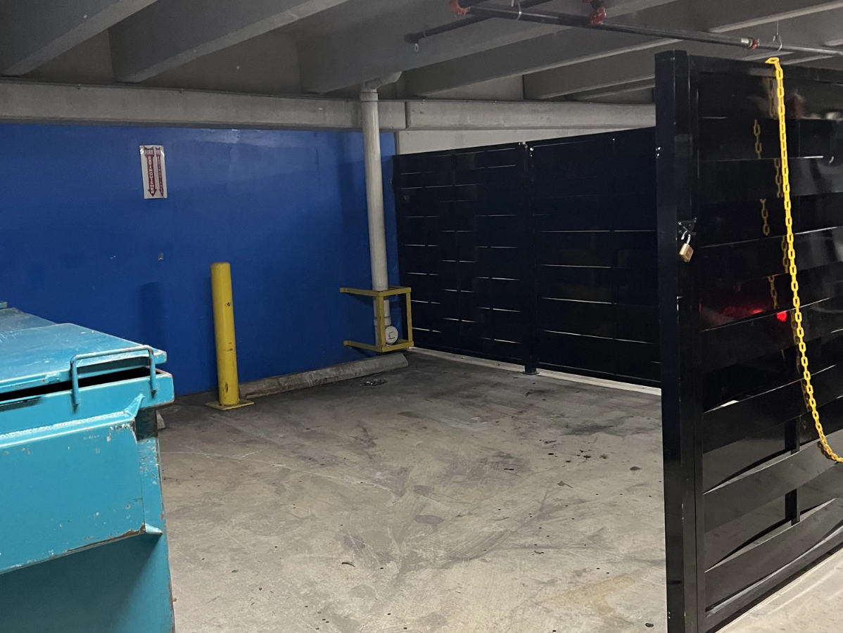 Dumpster enclosure in a parking garage; blue dumpster, black metal gate, blue wall, yellow post.