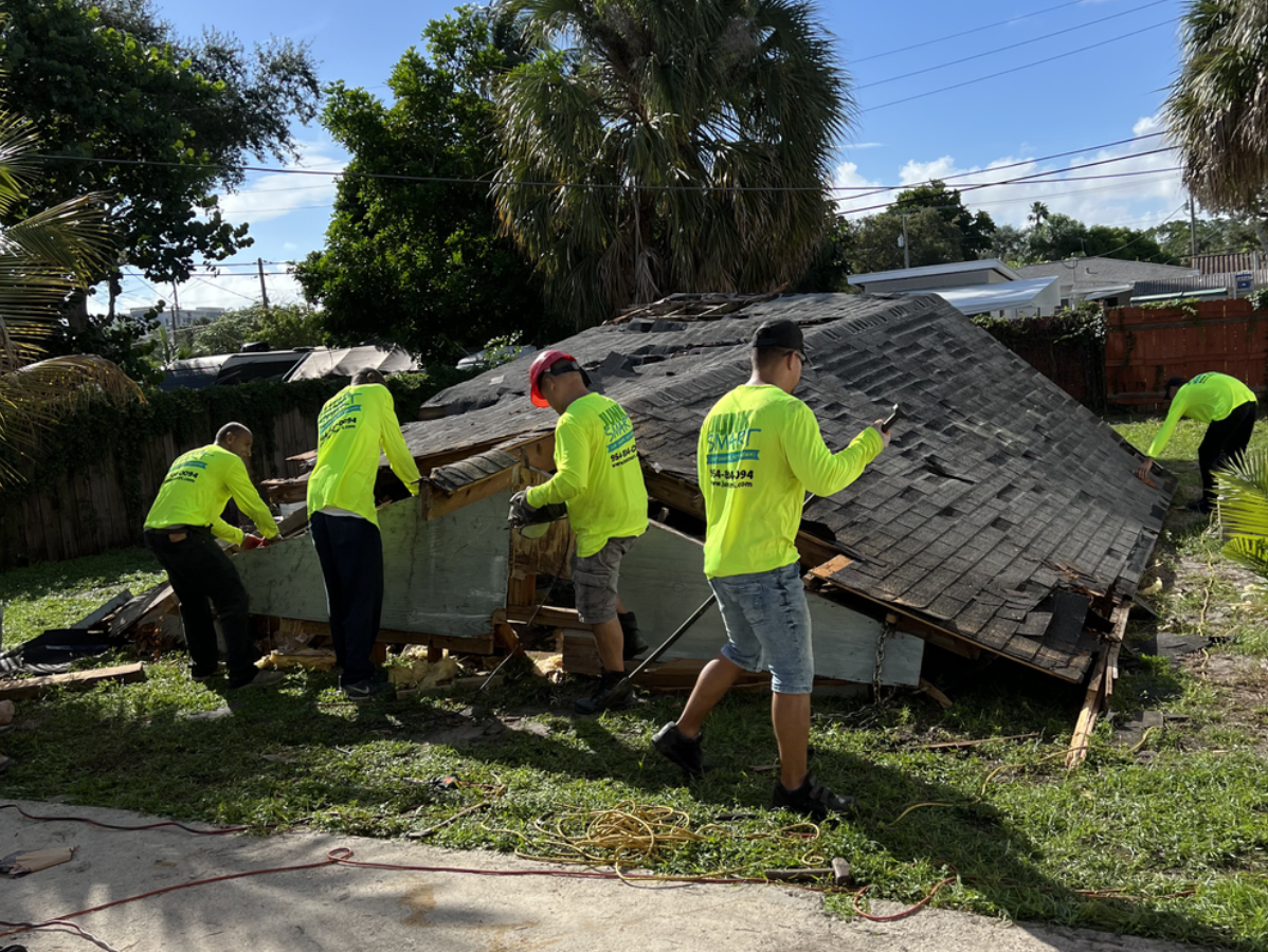 Construction workers in neon yellow shirts dismantle a damaged roof.