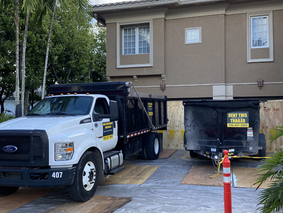 Dump truck and trailer parked next to a house under construction. Brown house with wooden beams.
