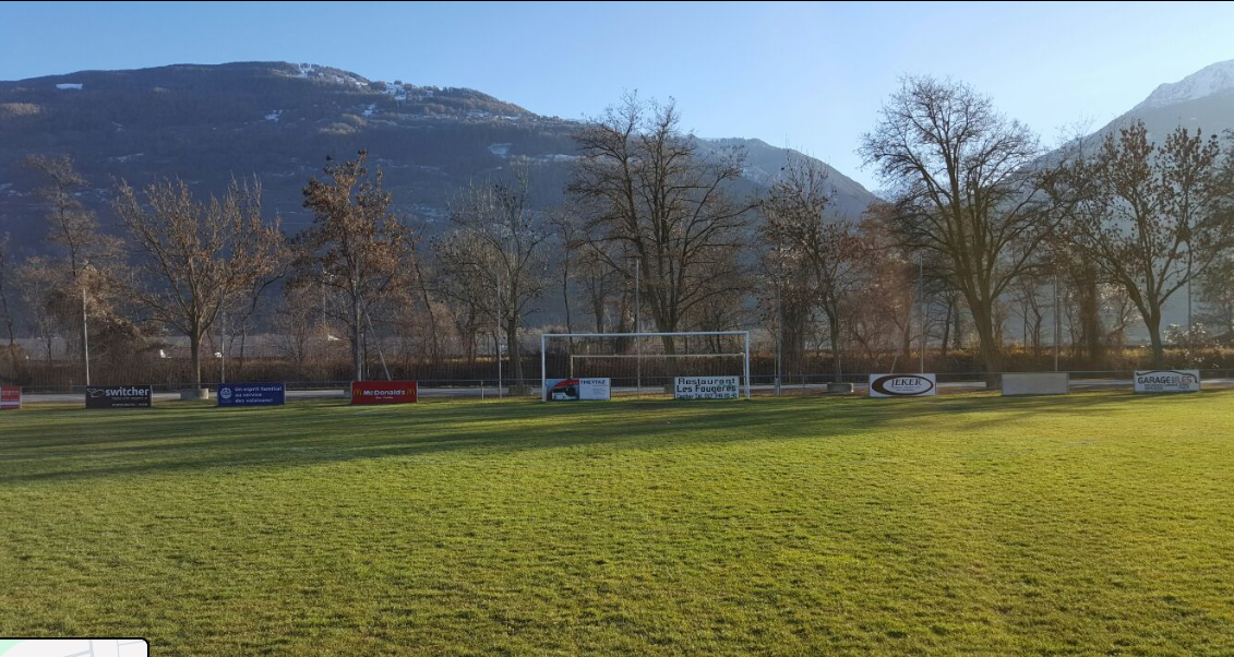 Un terrain de football avec des montagnes en arrière-plan et des arbres au premier plan.